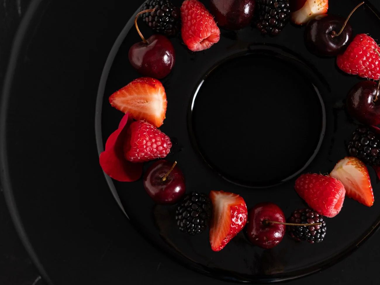 Assorted fresh berries, including strawberries, cherries, blackberries, and raspberries, arranged on a black circular tray.