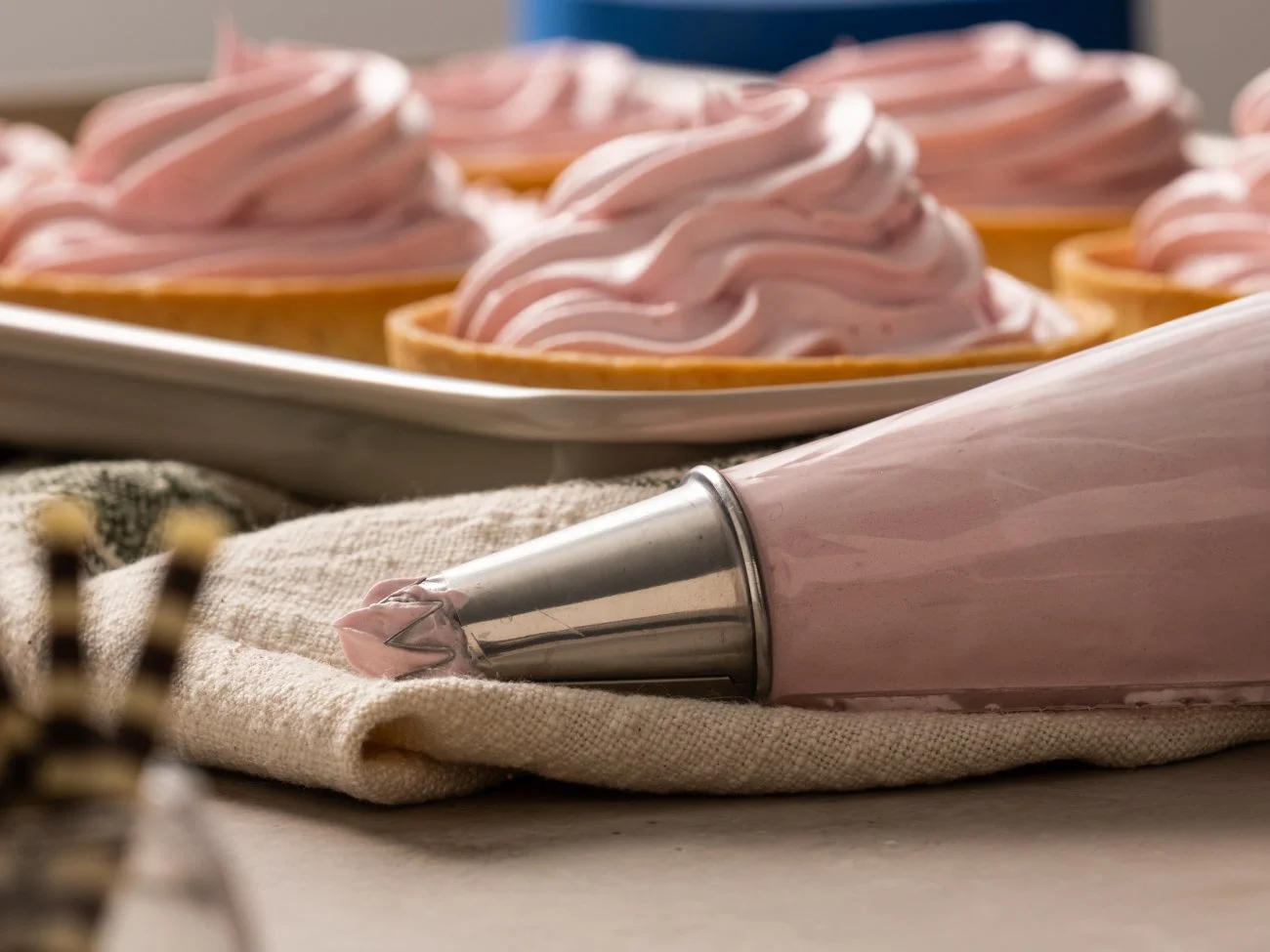 Pink frosting on cookies and a piping bag filled with pink frosting resting on a cloth.