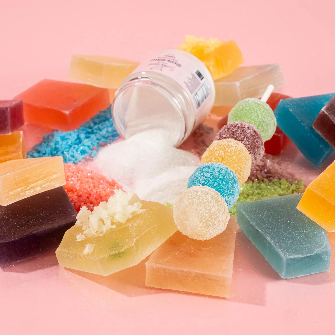 Colorful assortment of soap bars, salt, and sugar candies on pink background
