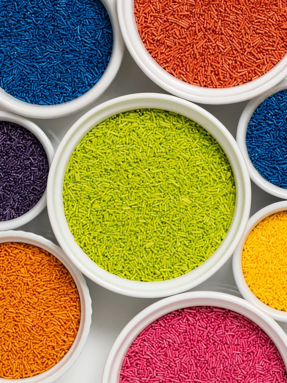 Colorful bowls filled with various colored sprinkles, including shades of blue, orange, yellow, pink, purple, and green.