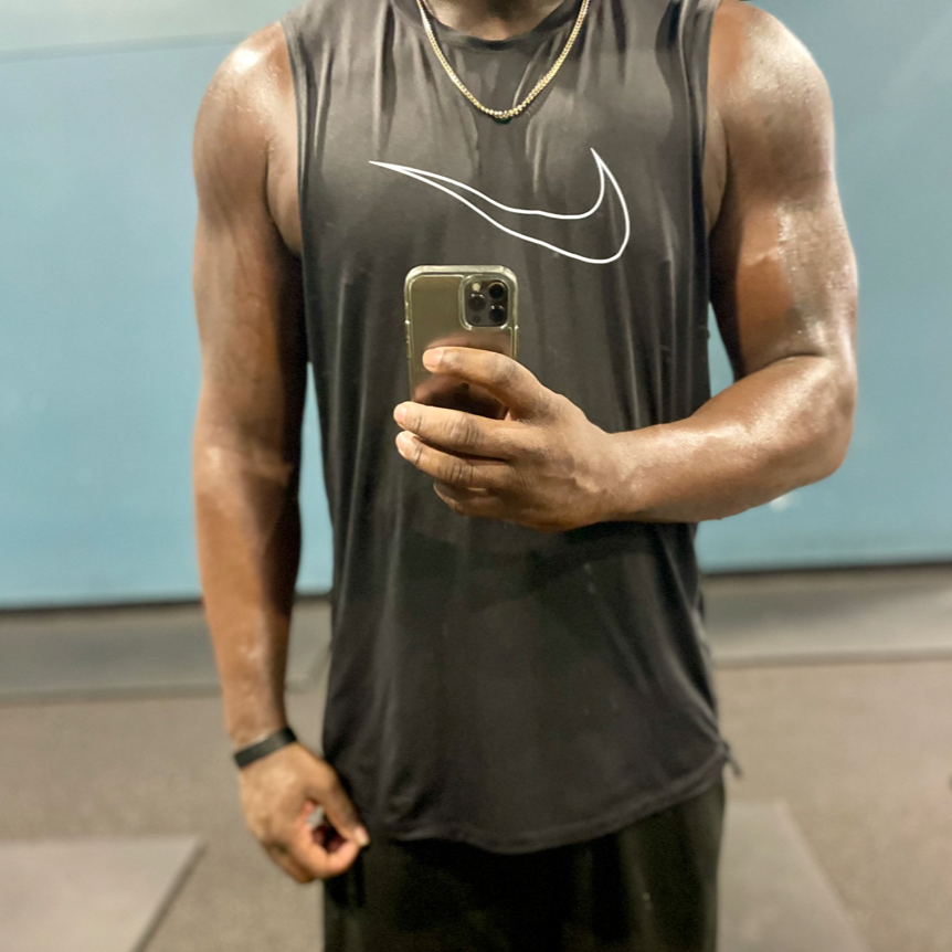 A man taking a mirror selfie at the gym, wearing a black Nike sleeveless athletic shirt and gold necklace.
