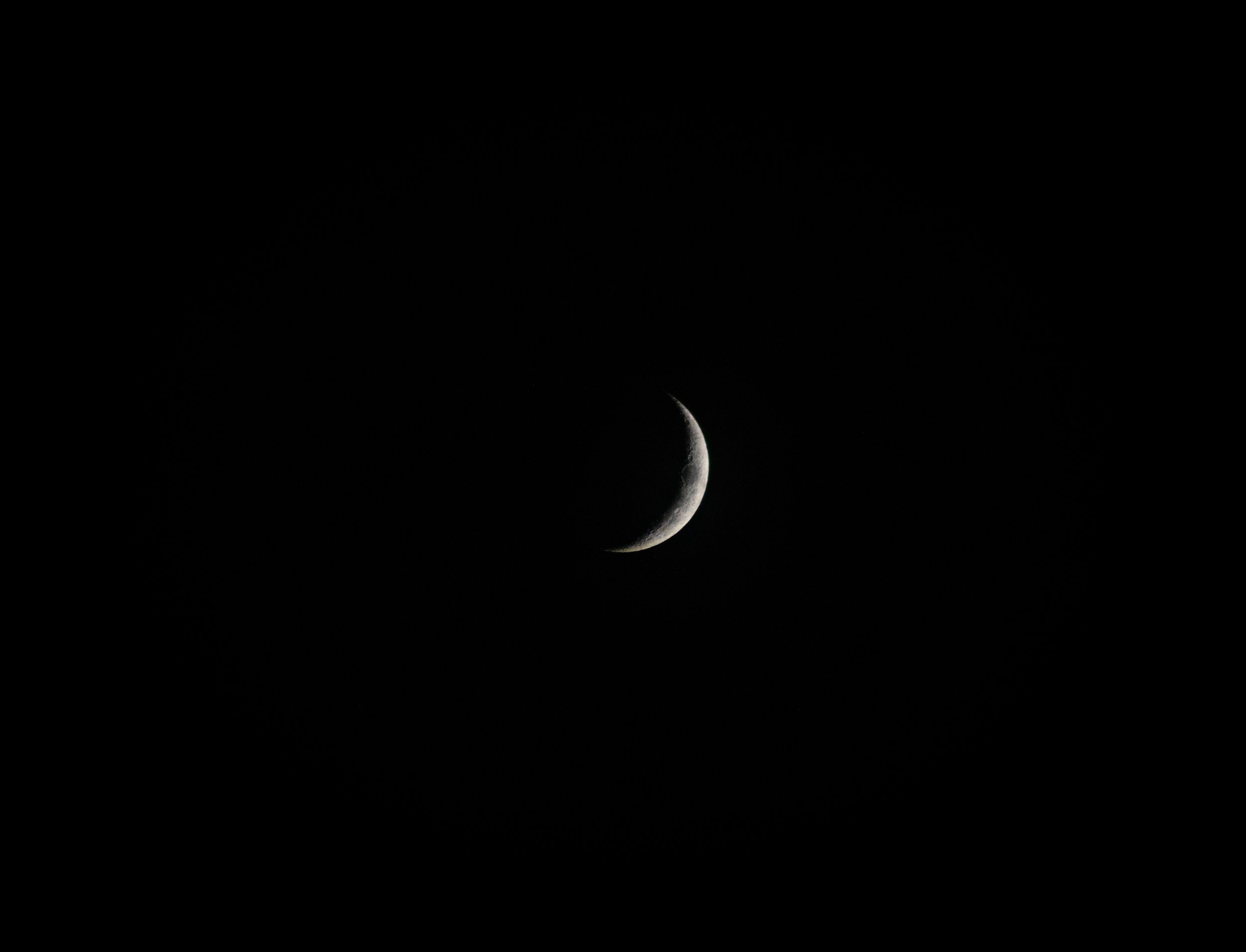 A crescent moon in the night sky with no visible stars.