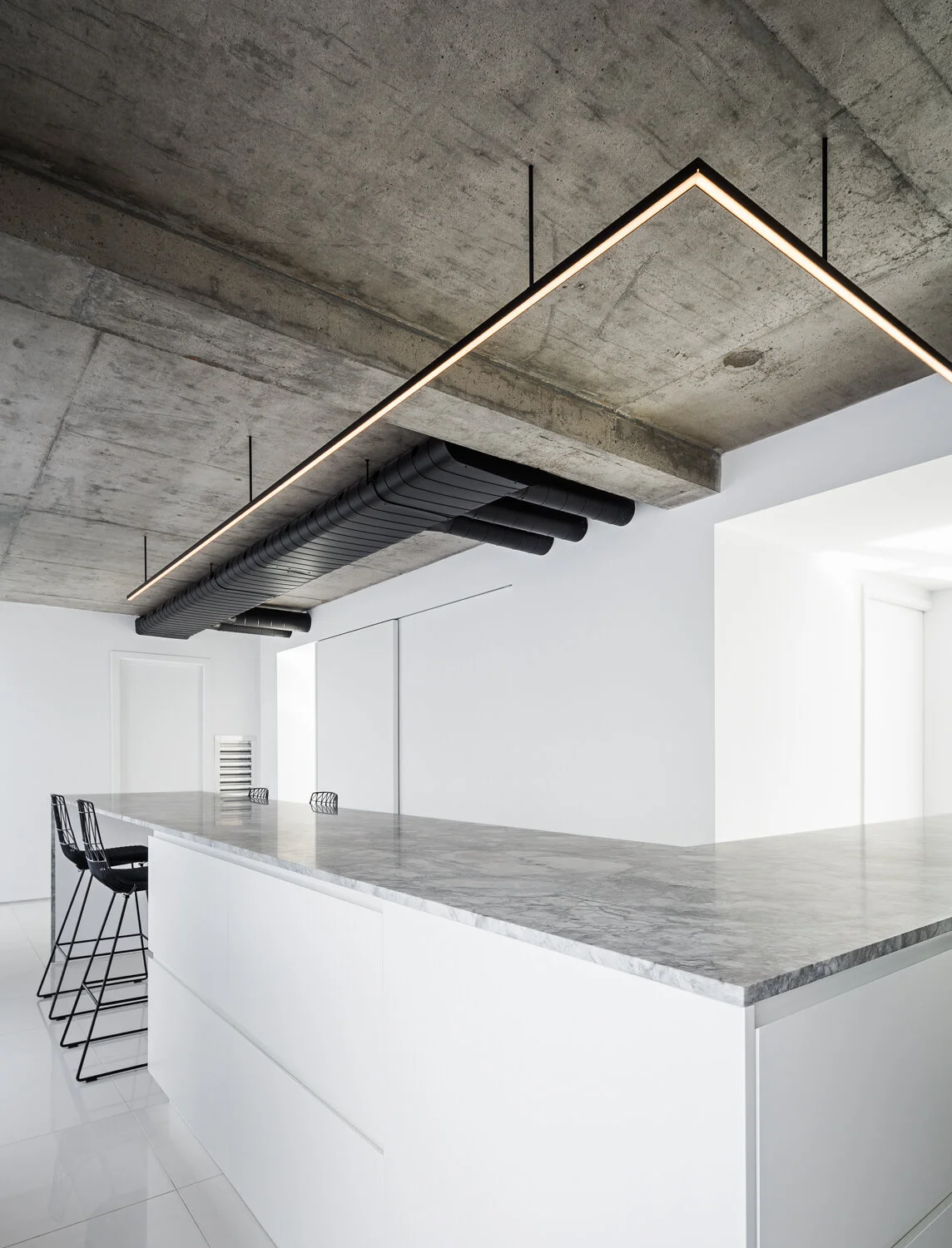 L-shaped kitchen with very large ¾ ”statuario marble countertop honed finish. Section with black stools Lucy from Bend Goods. Satin white lacquer finished kitchen cabinets and concrete ceiling