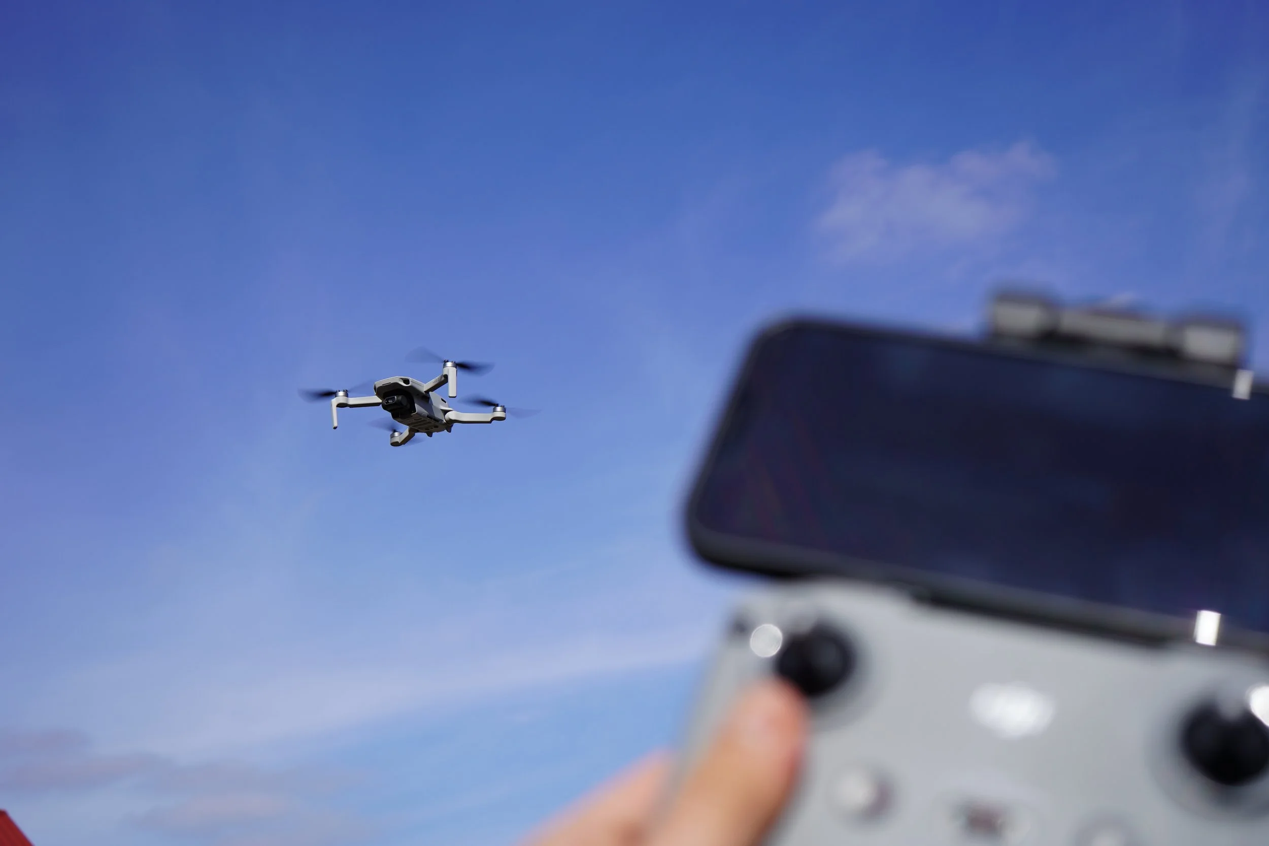 A drone flying in the sky and a person holding a remote control in the foreground.