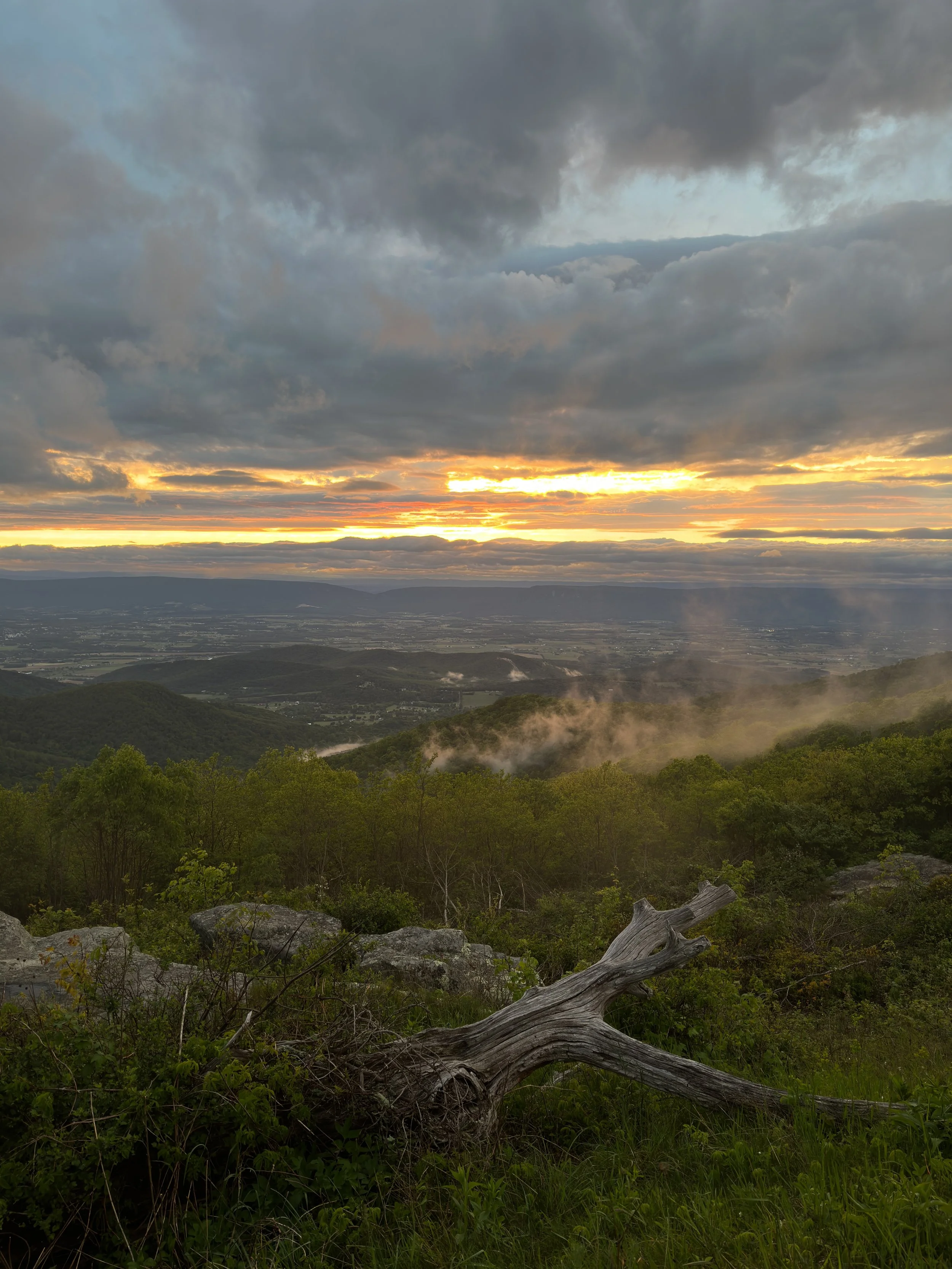 Sunset over mountains with cloudy sky and smoke rising from the forest.
