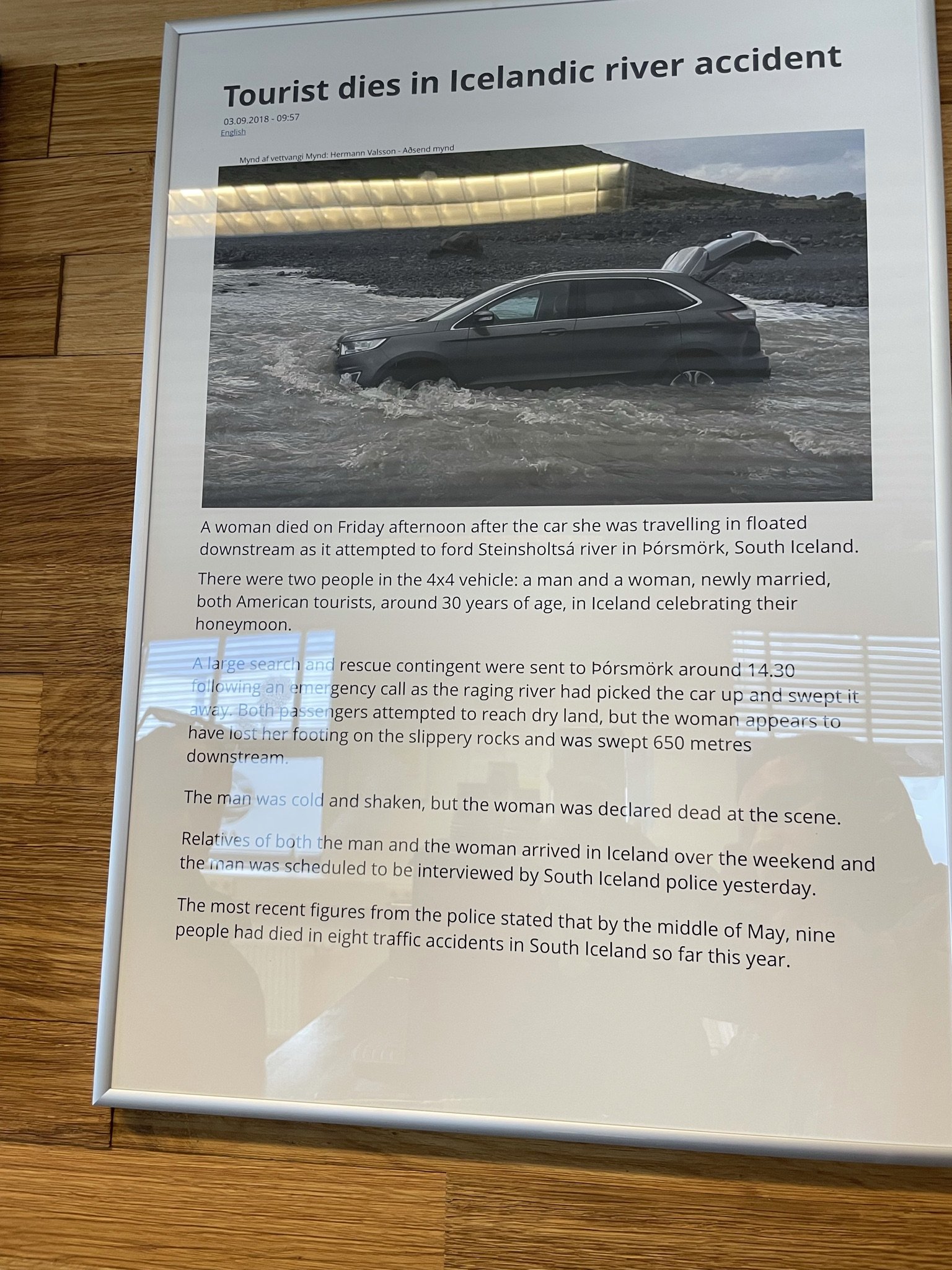 A newspaper article with the headline 'Tourist dies in Icelandic river accident', showing a photo of a black car submerged in a flooded river, with its rear hatch open.