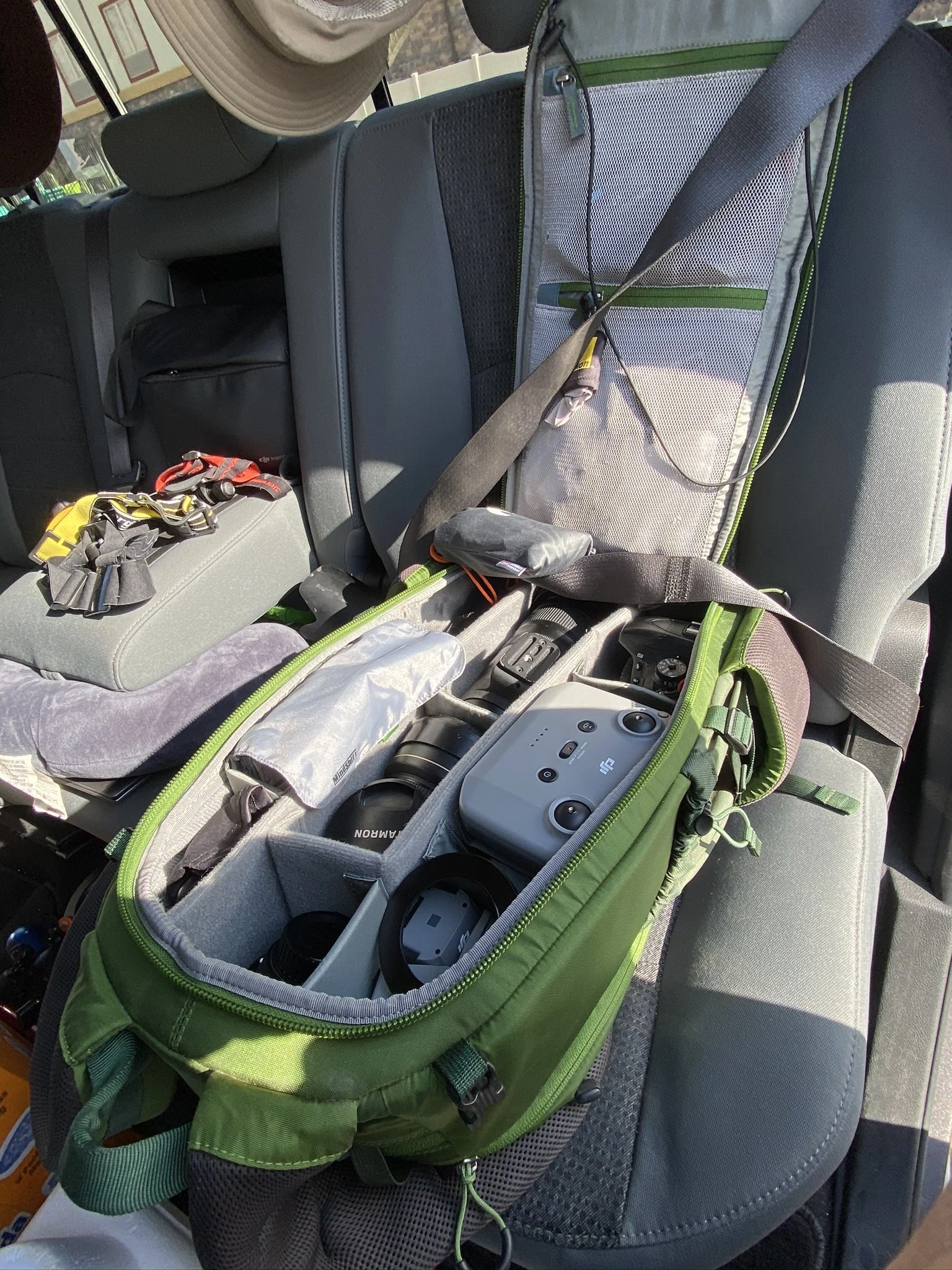 Camera gear and accessories packed inside a green bag on the back seat of a vehicle.