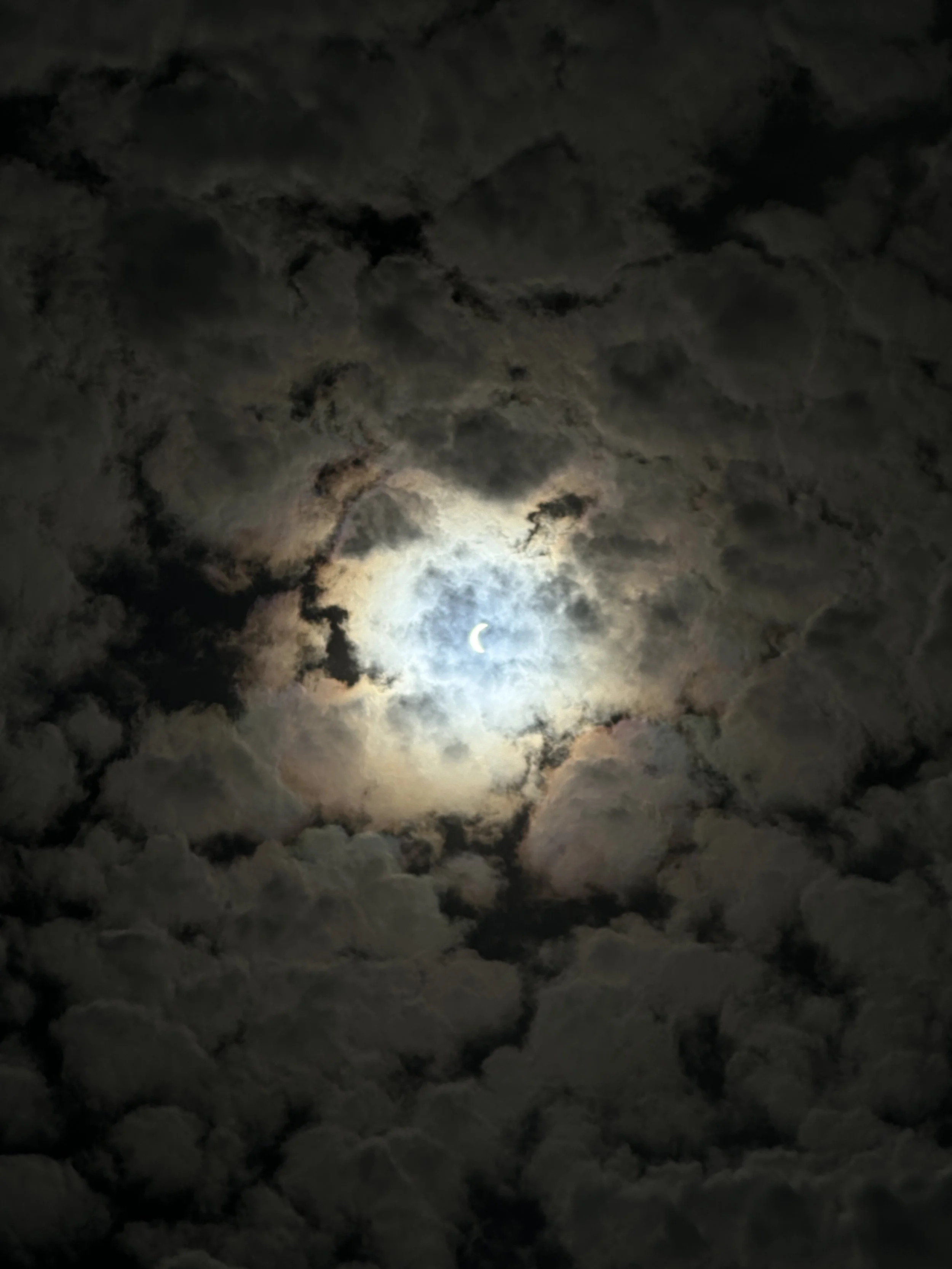 Night sky with a crescent moon partially obscured by dark, thick clouds.