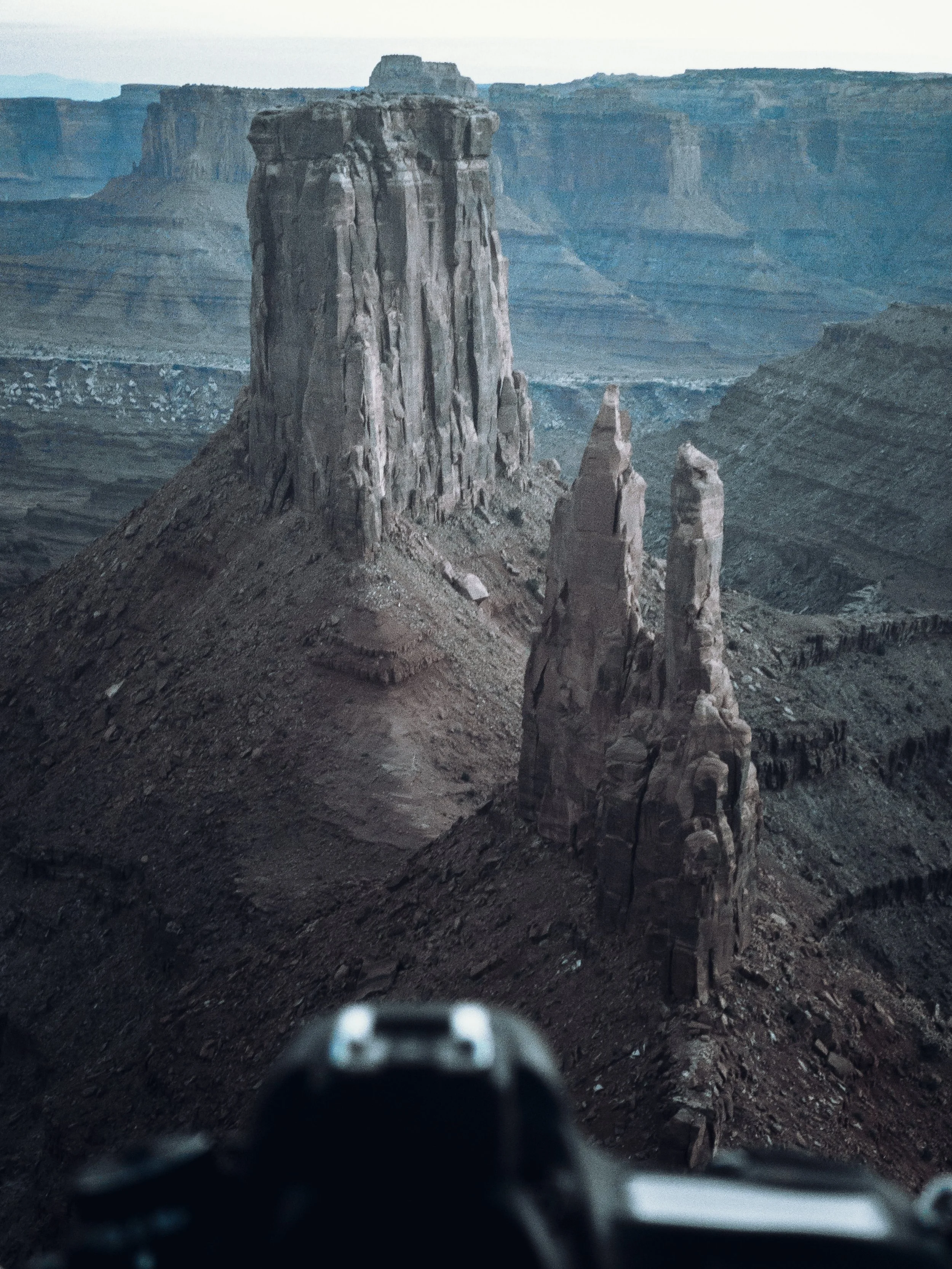 A view of a canyon with tall rock formations, seen from the perspective of a person on a motorcycle or vehicle, with mountains in the background.
