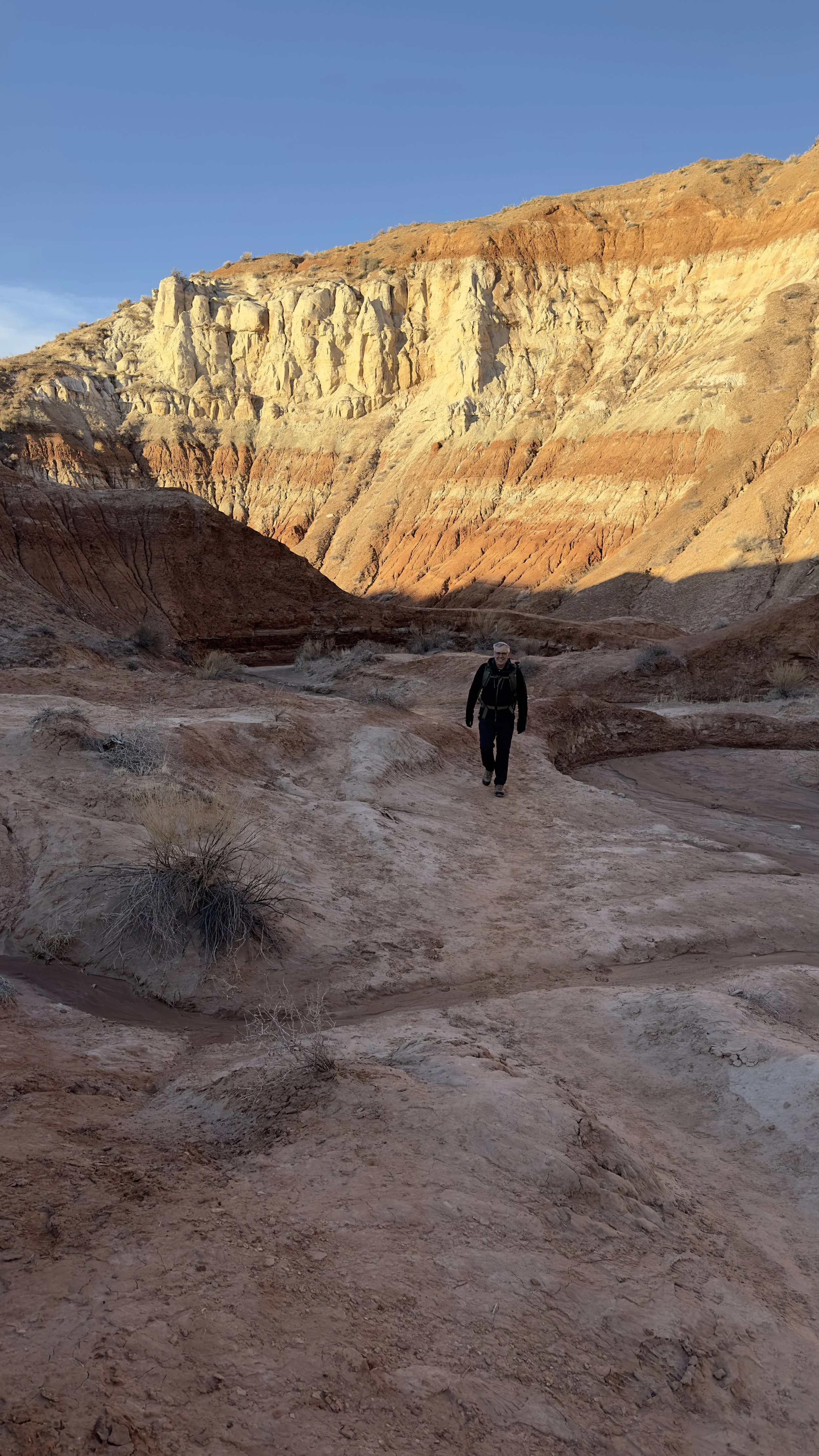 A person hiking in a desert canyon with layered rock formations and clear blue sky