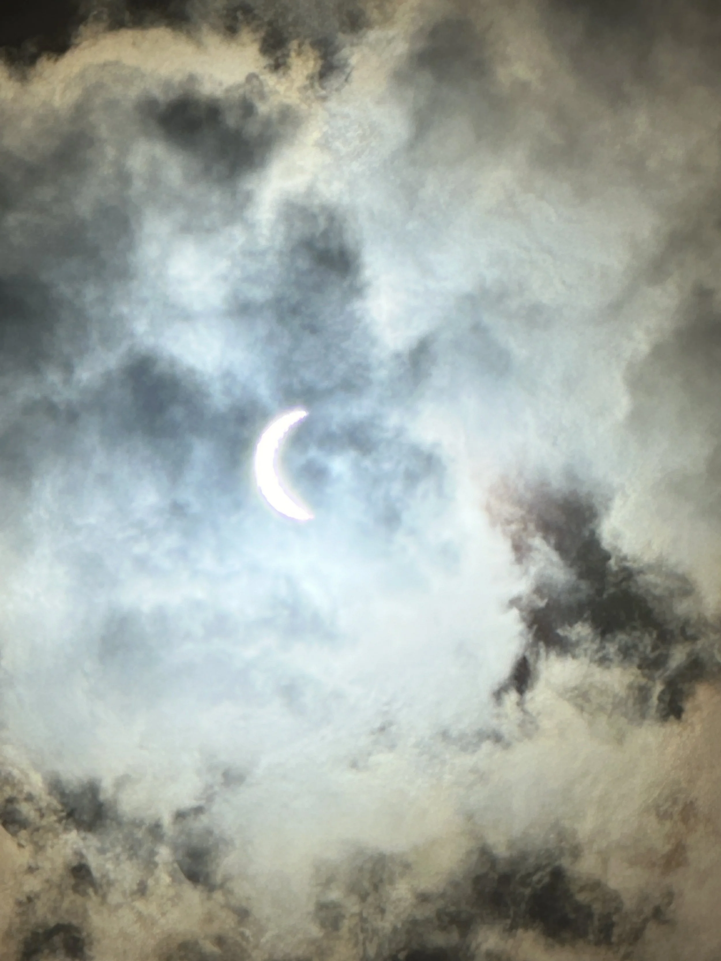 Partial moon shining through dark, cloudy sky at night.