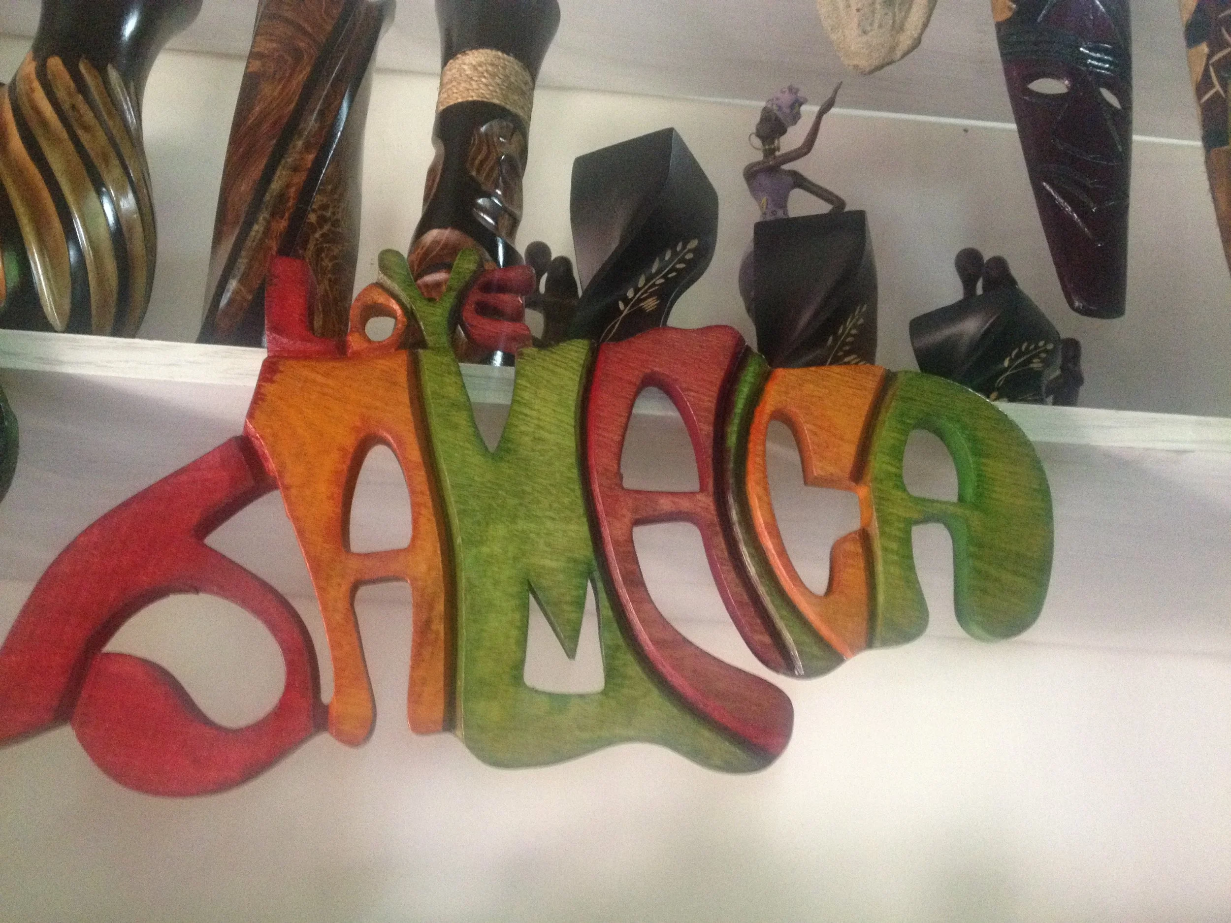 Colorful wooden sculpture spelling 'LOVE' in red, orange, and green, with background of black and brown carved wooden masks.