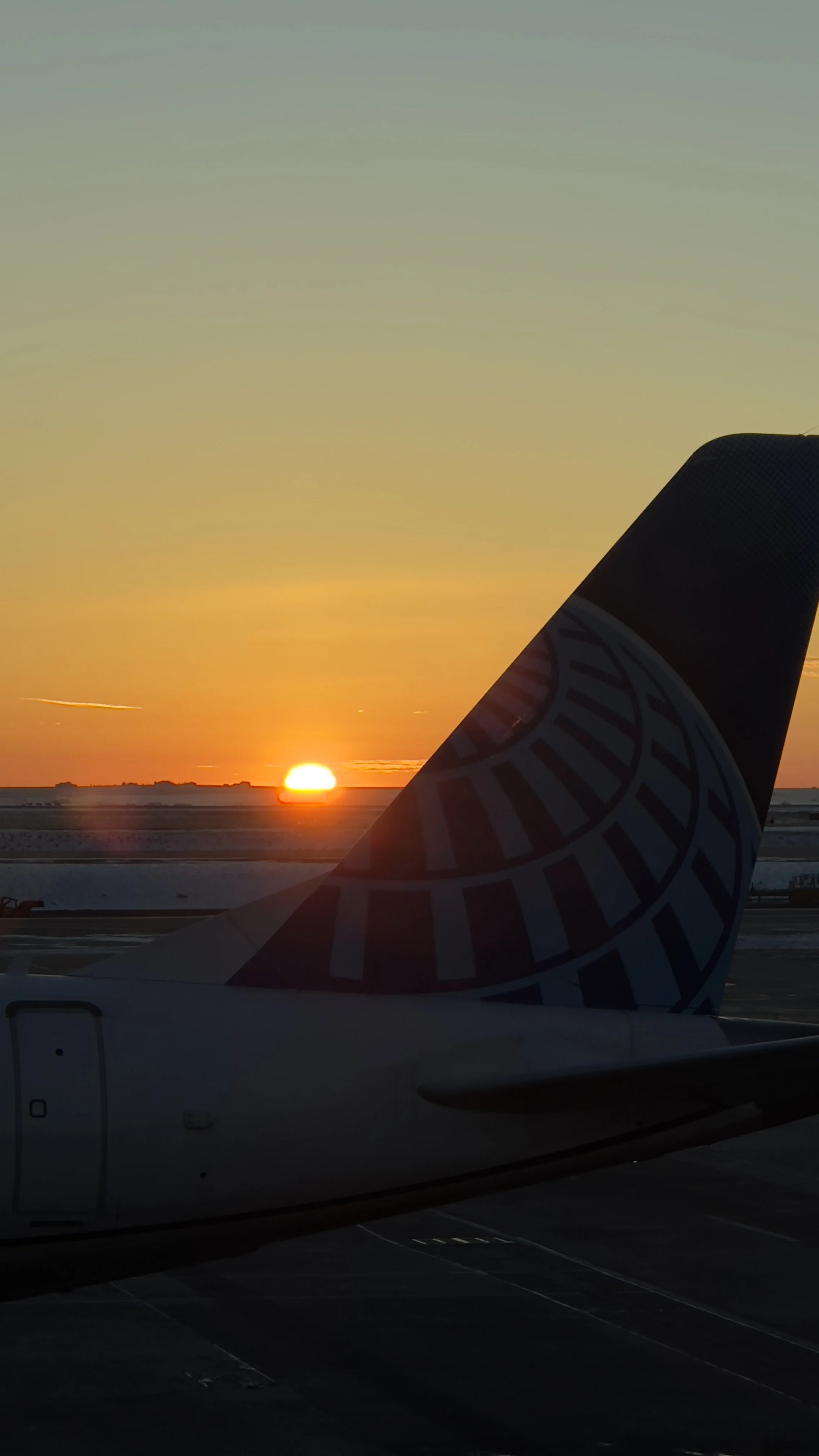 Sunset behind an airplane's tailfin at an airport runway.