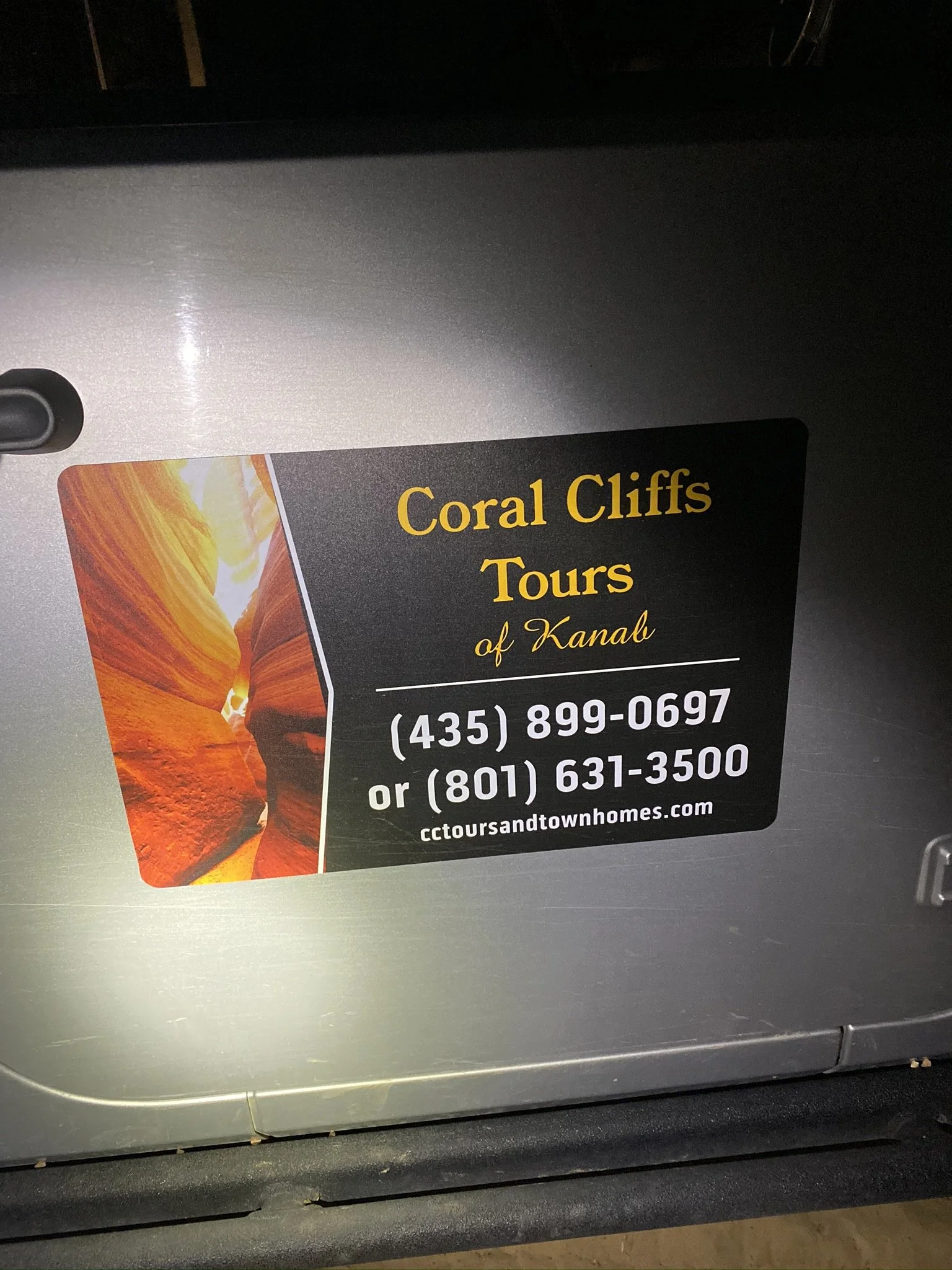 A sticker on a machine advertising Coral Cliffs Tours of Kanab, with phone numbers and website
