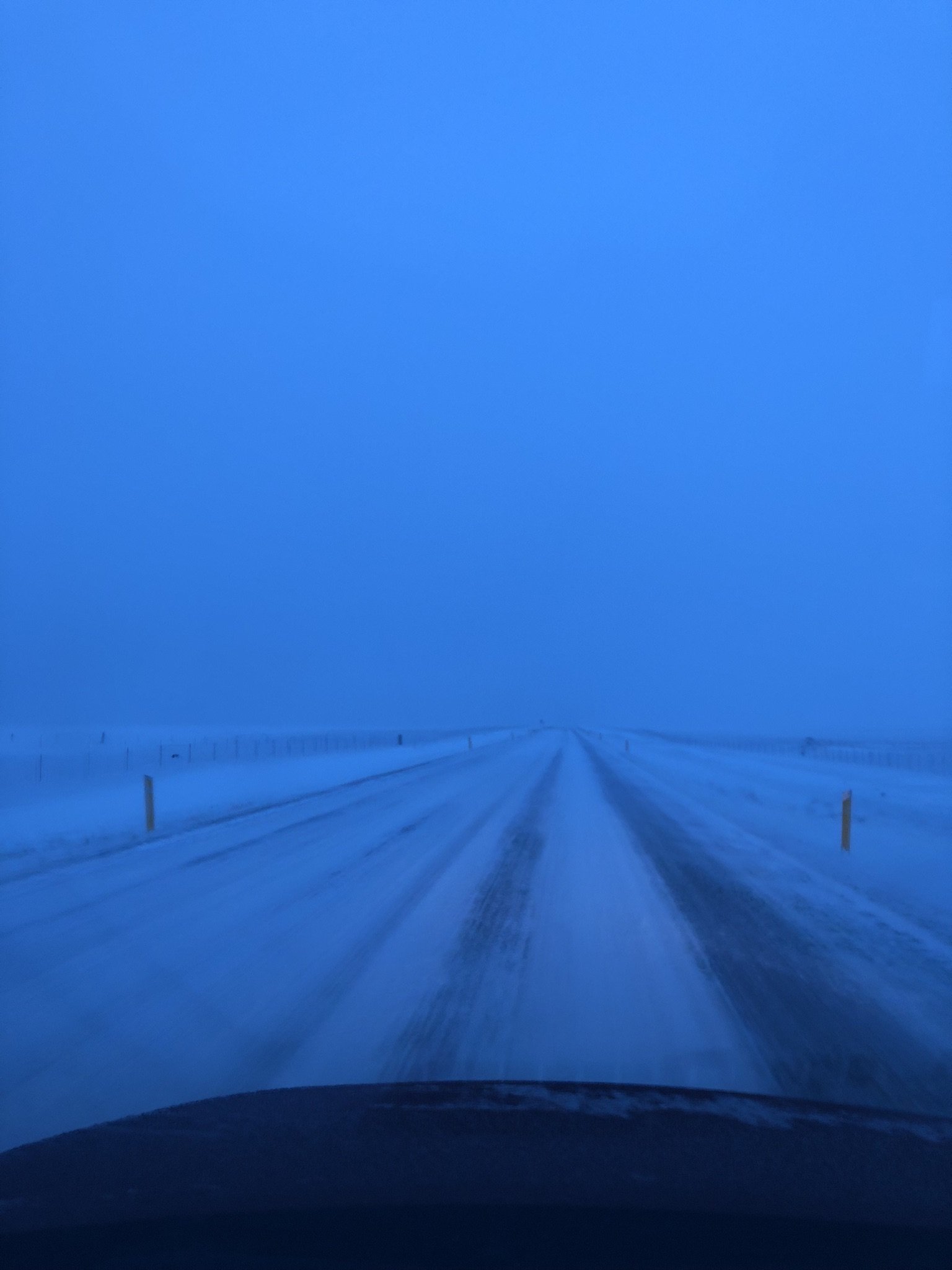 Snow-covered road stretching into the foggy distance under a blue sky.