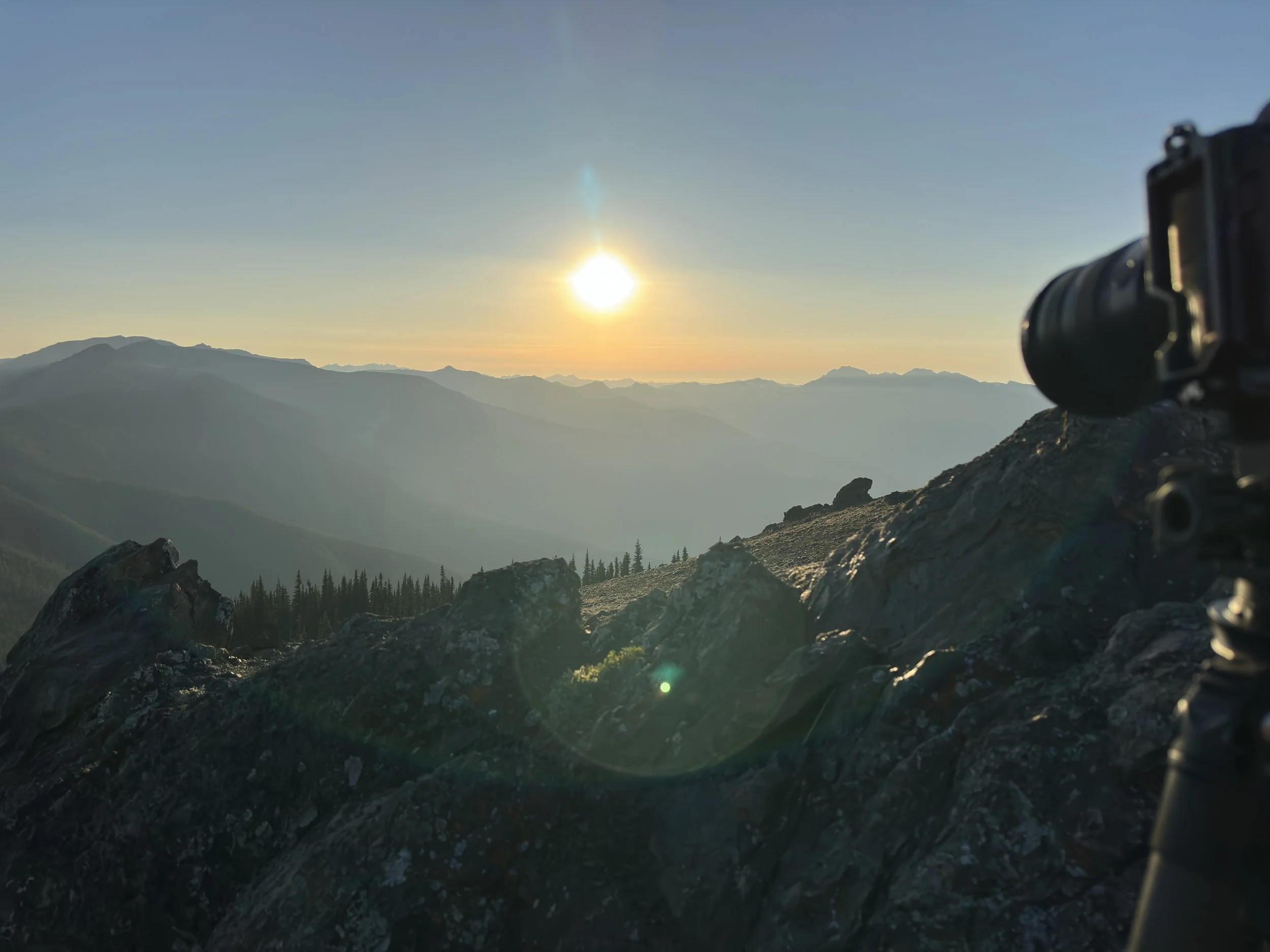 A camera set on rocks capturing a scenic mountain landscape during sunset, with layers of distant mountains and a clear sky.