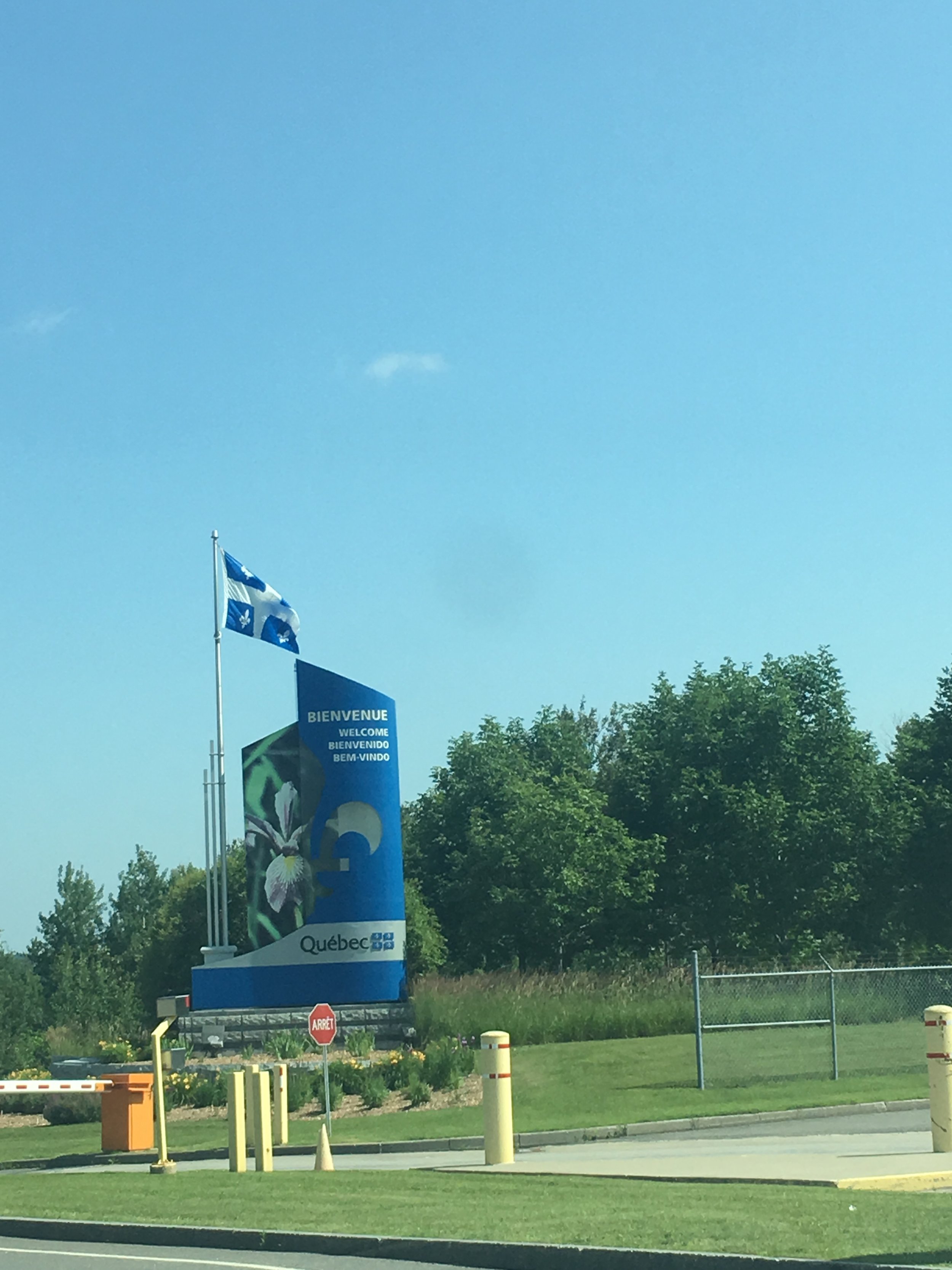 Welcome sign for Quebec with flags and trees in the background.