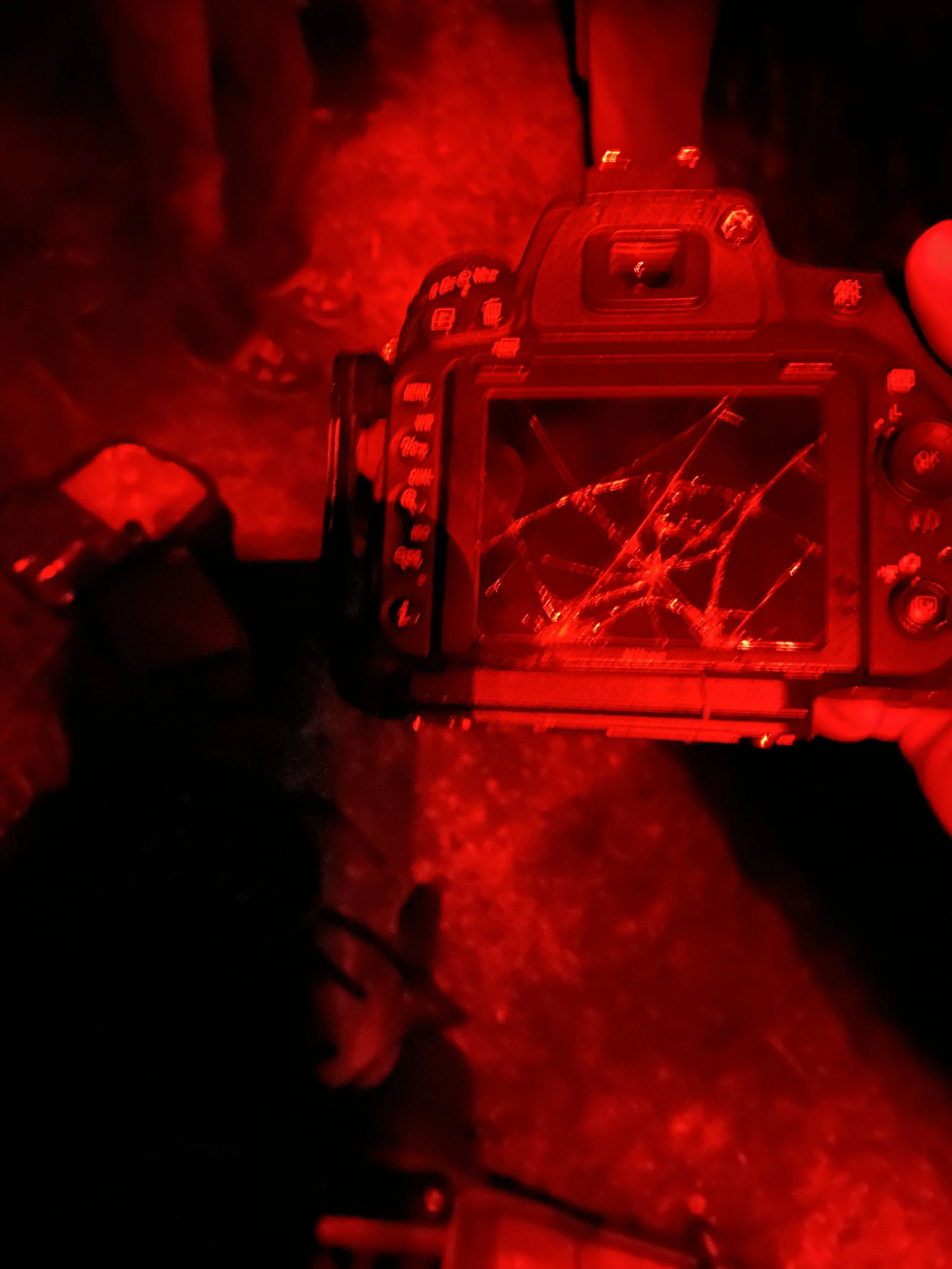 Camera with a shattered screen, illuminated by red light, on a dark surface.