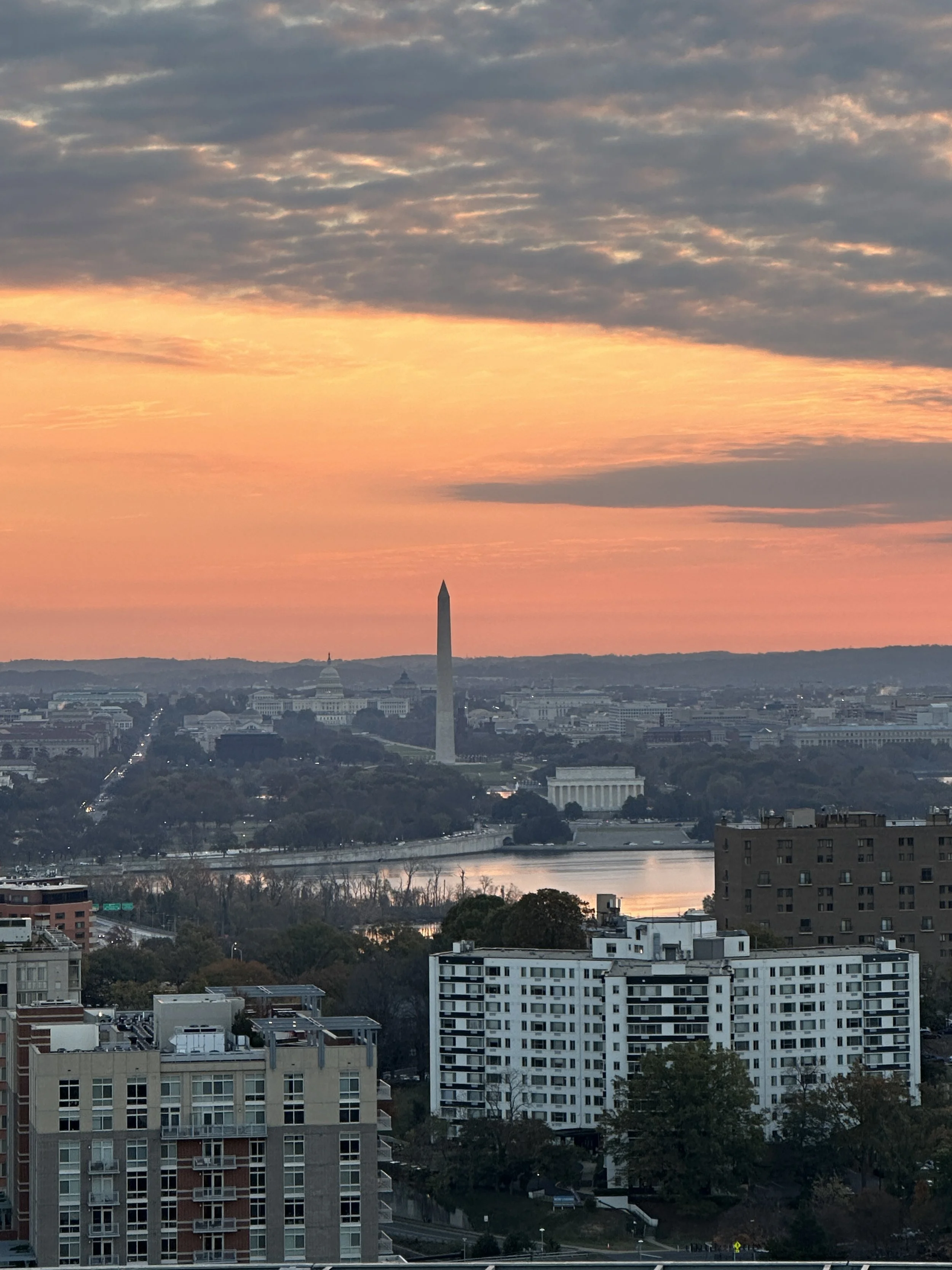Sunset over Washington, D.C. skyline, featuring the Washington Monument and other historic buildings near the Potomac River.