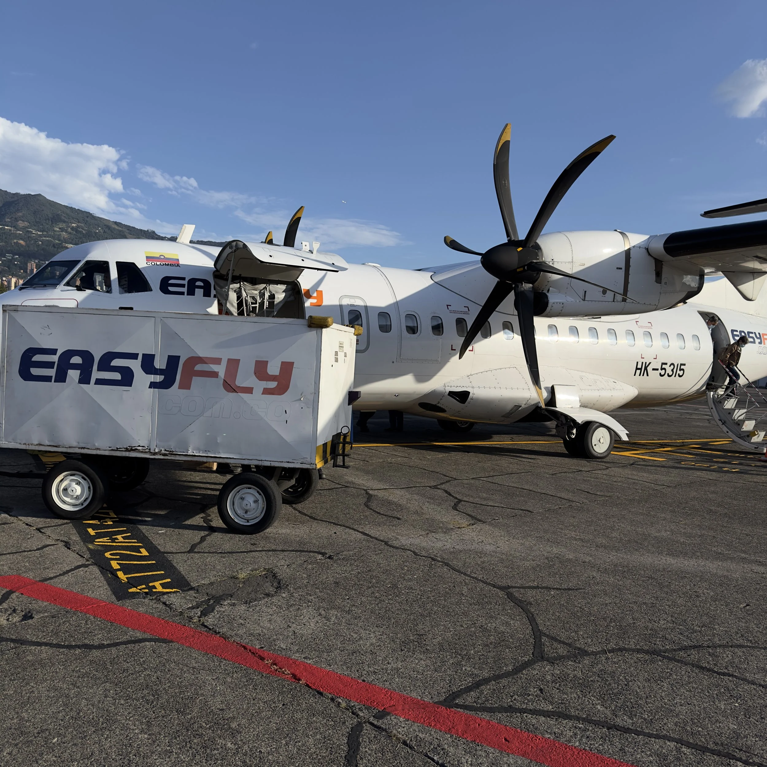 Small white passenger airplane at the airport on a sunny day, with taxiing markings on the cracked tarmac surface.
