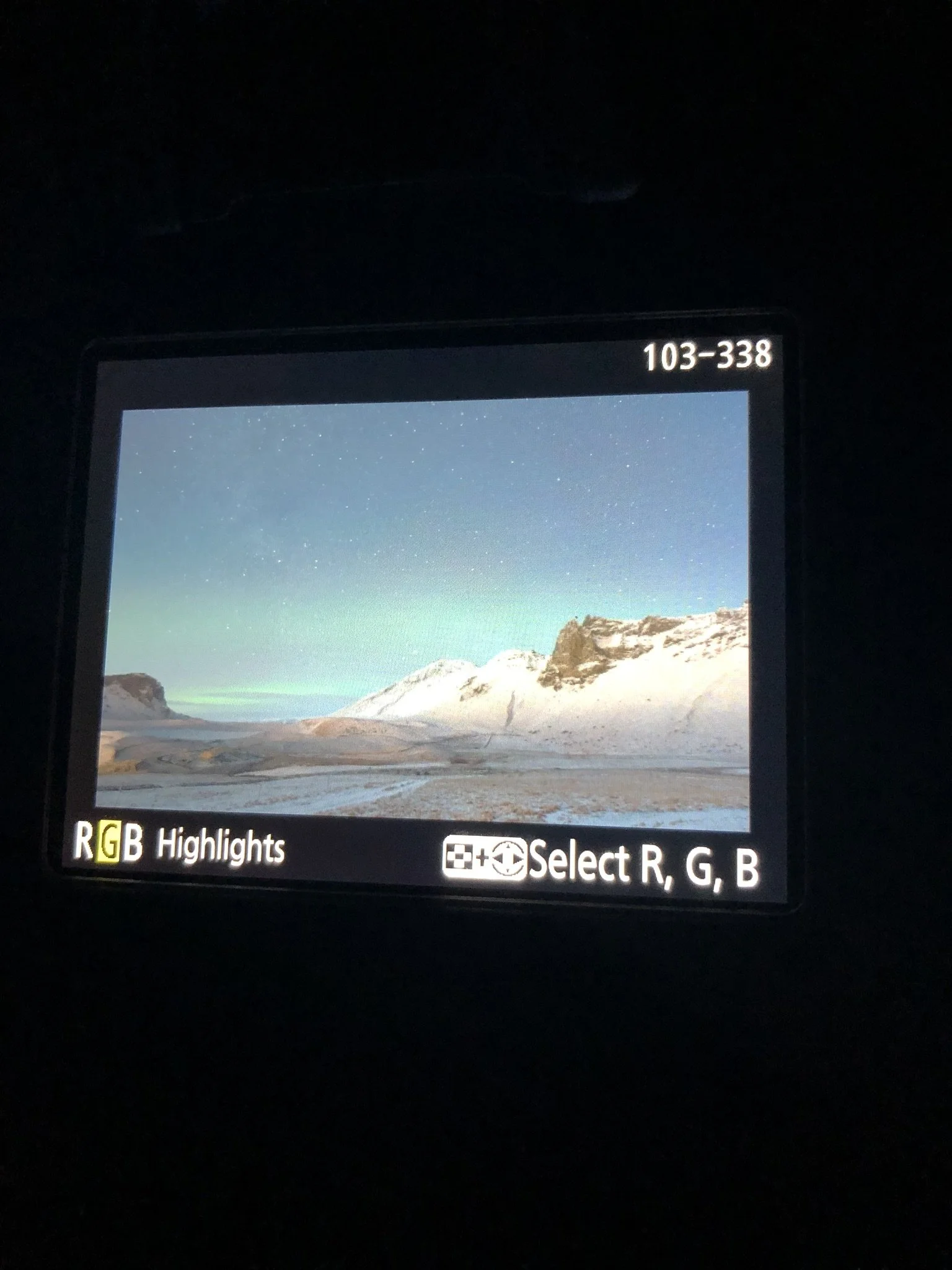 Camera display showing a snowy mountain landscape under a starry sky with visible northern lights.