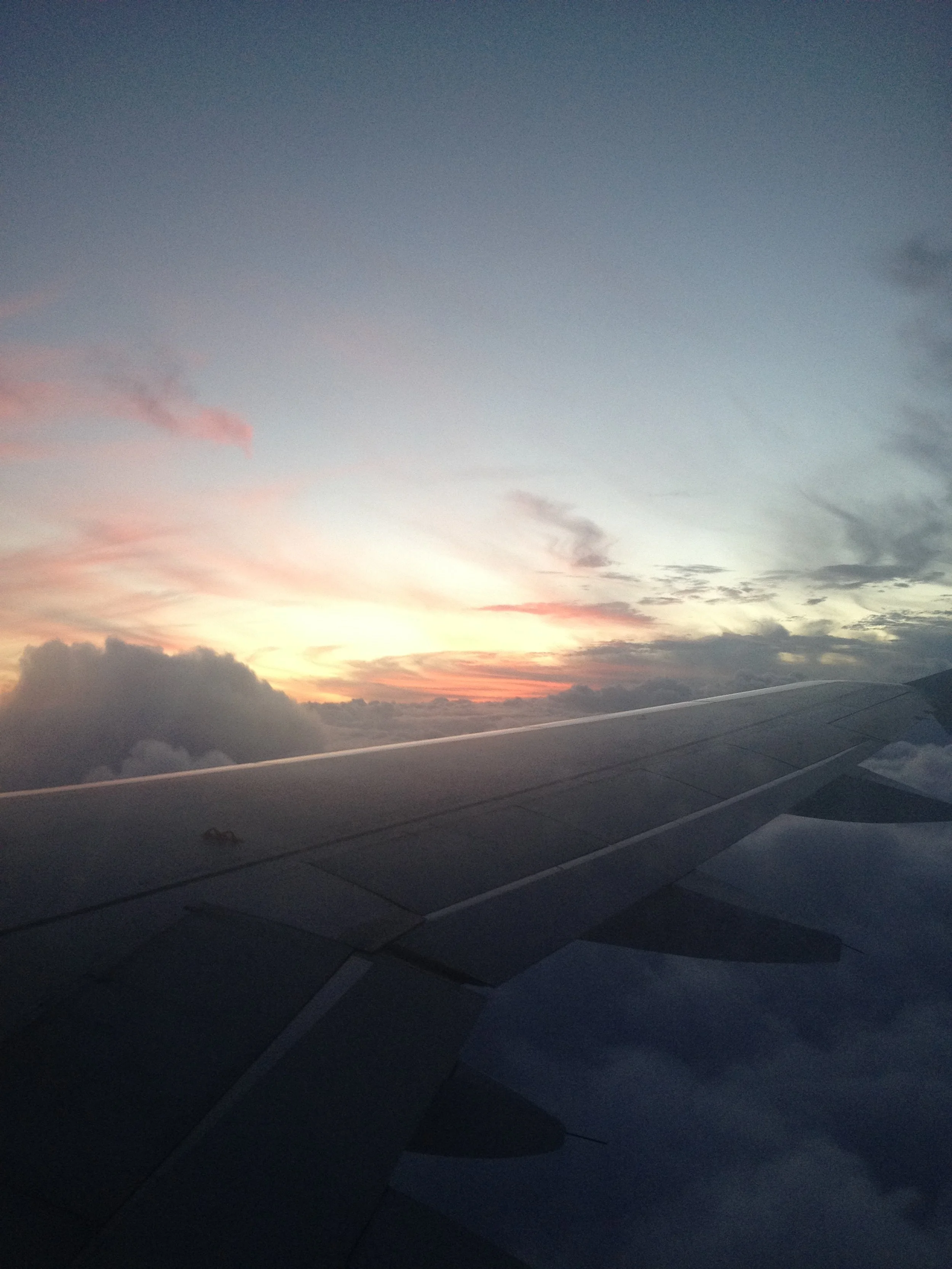View from airplane window showing wing and a sunset sky with clouds.