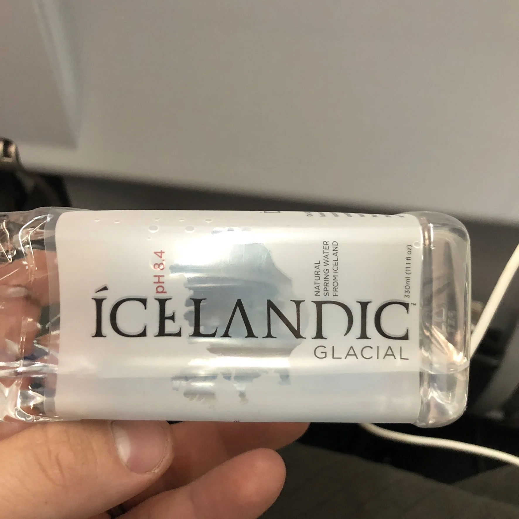 A person holding a bottle of Icelandic Glacial spring water with a white label, black text, and a graphic of an iceberg.