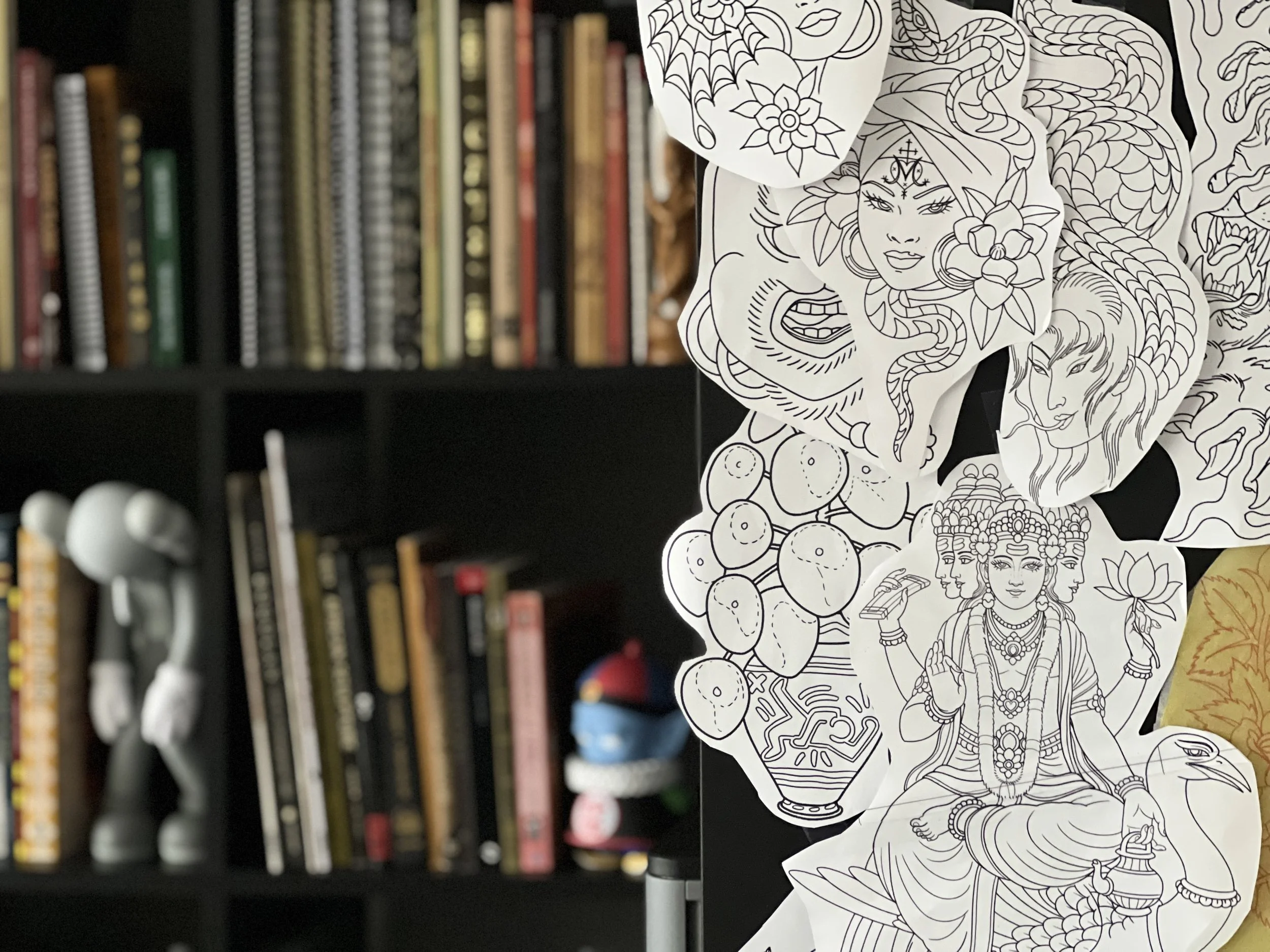 Collection of drawings in a variety of tattoo styles at Lightwork Tattoo, bookshelf full of books on different tattoo stylesc can be seen out of focus in the background