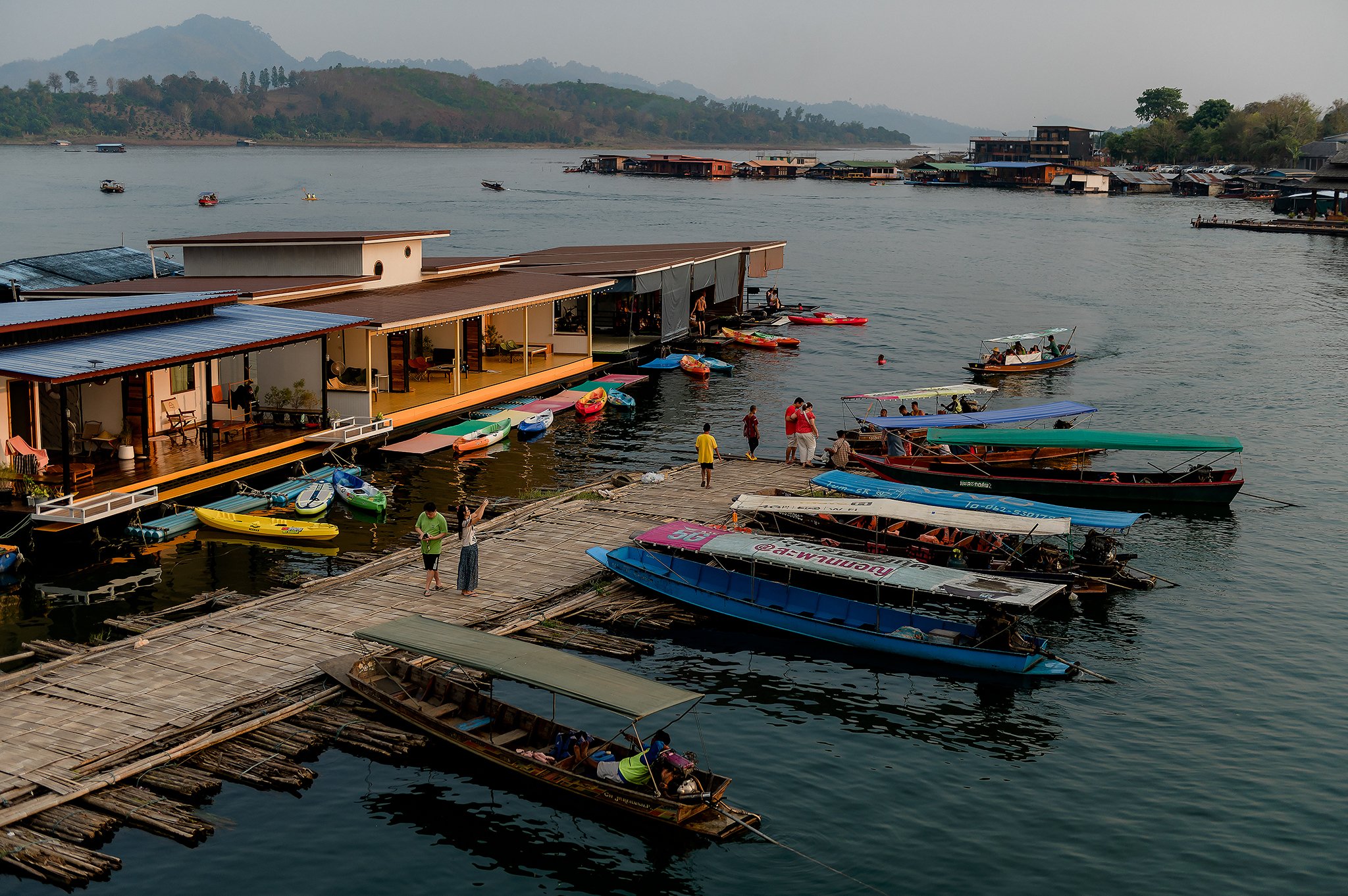 Wooden boat docked at P. Guest House resort pier on Khao Laem Lake surrounded by lush greenery and calm water.