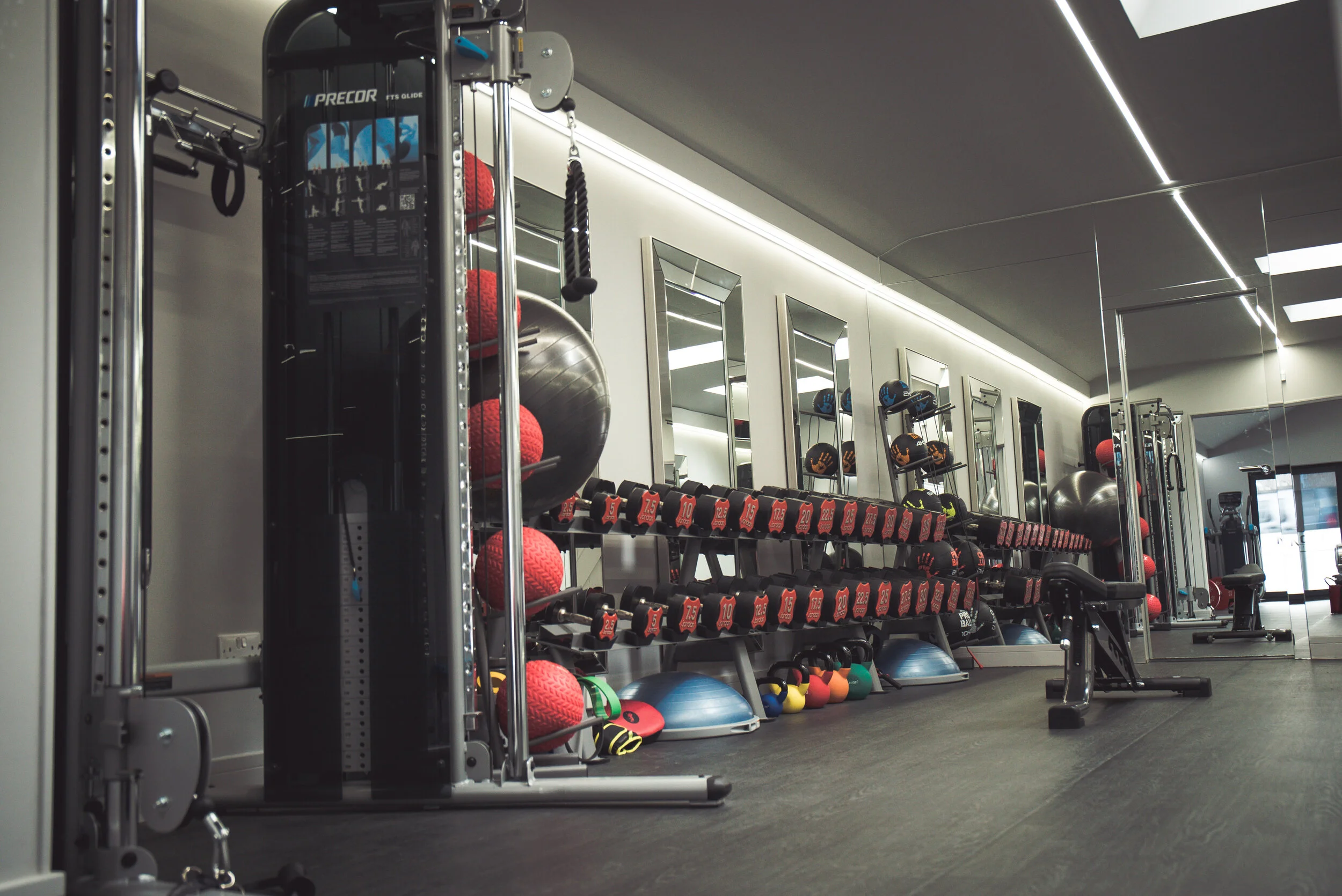 Modern gym with cable machine, dumbbell racks, kettlebells, medicine balls, exercise balls, and mirrored walls