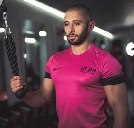 Muscular man in a pink NEON T-shirt exercising with a rope cable machine in a gym