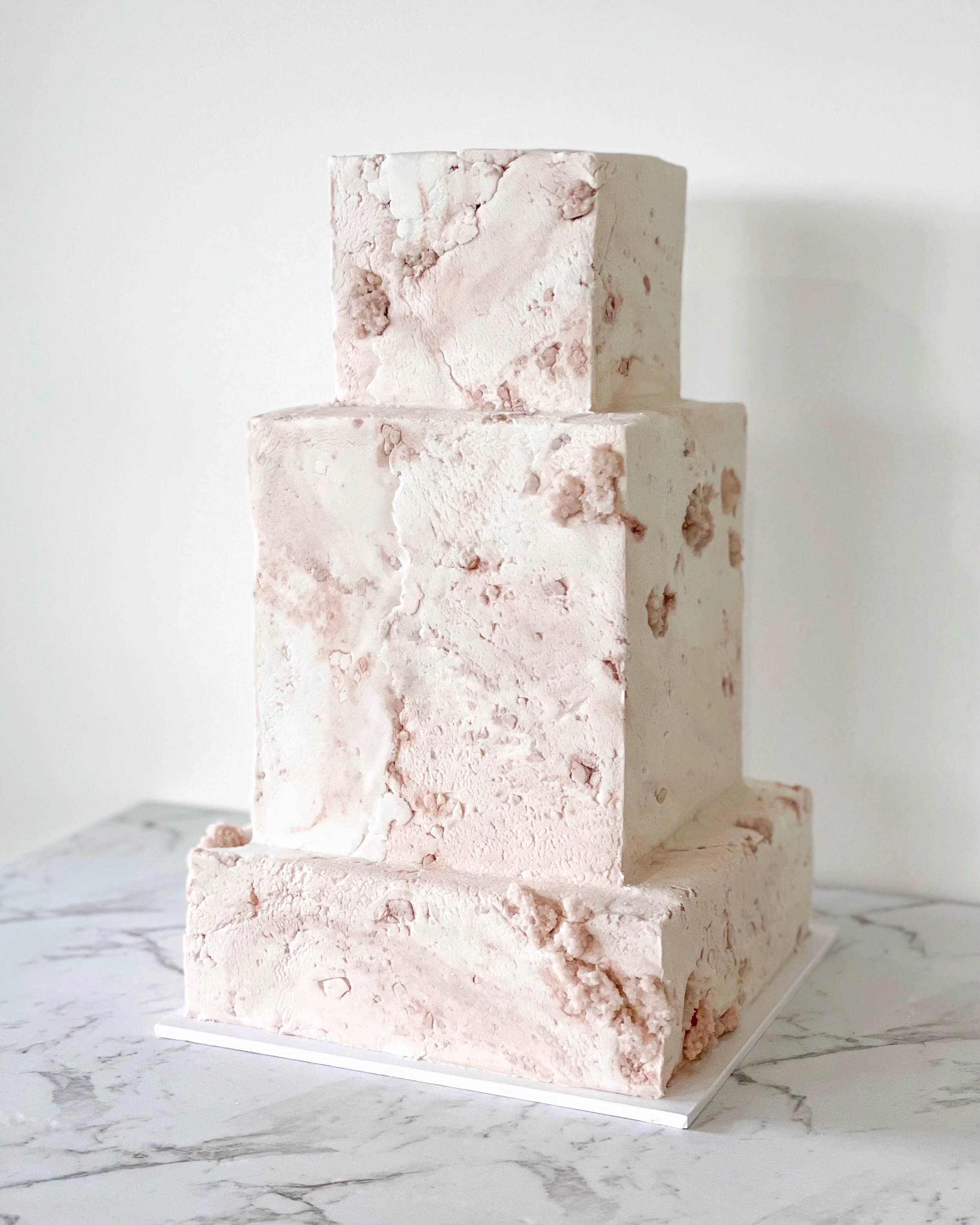 Three-tiered textured square cake on marble surface
