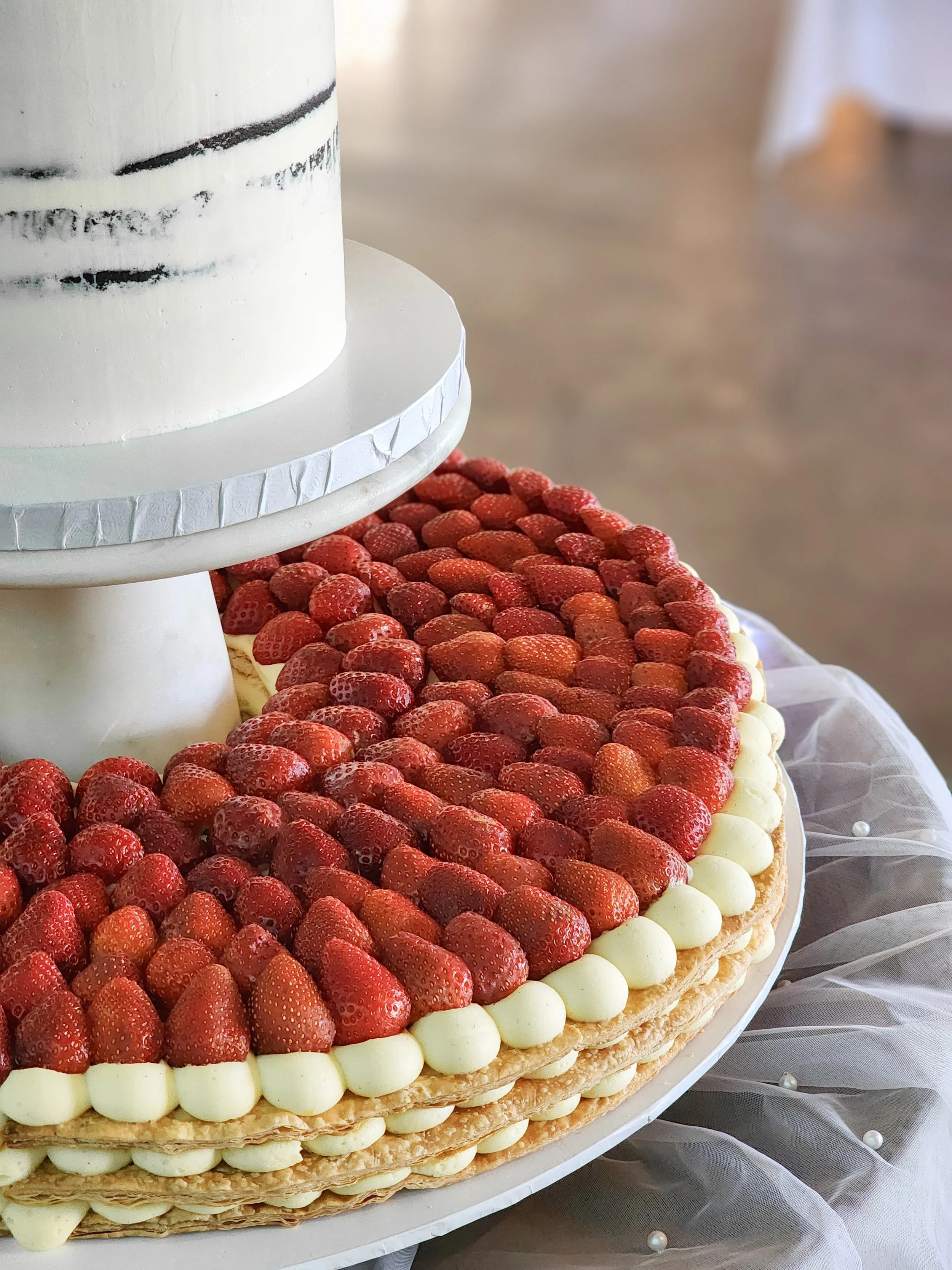 A layered European Millefoglie / Millefeuille pastry cake decorated with strawberries and custard patisserie cream on a white platter at a French / Italian inspired wedding.