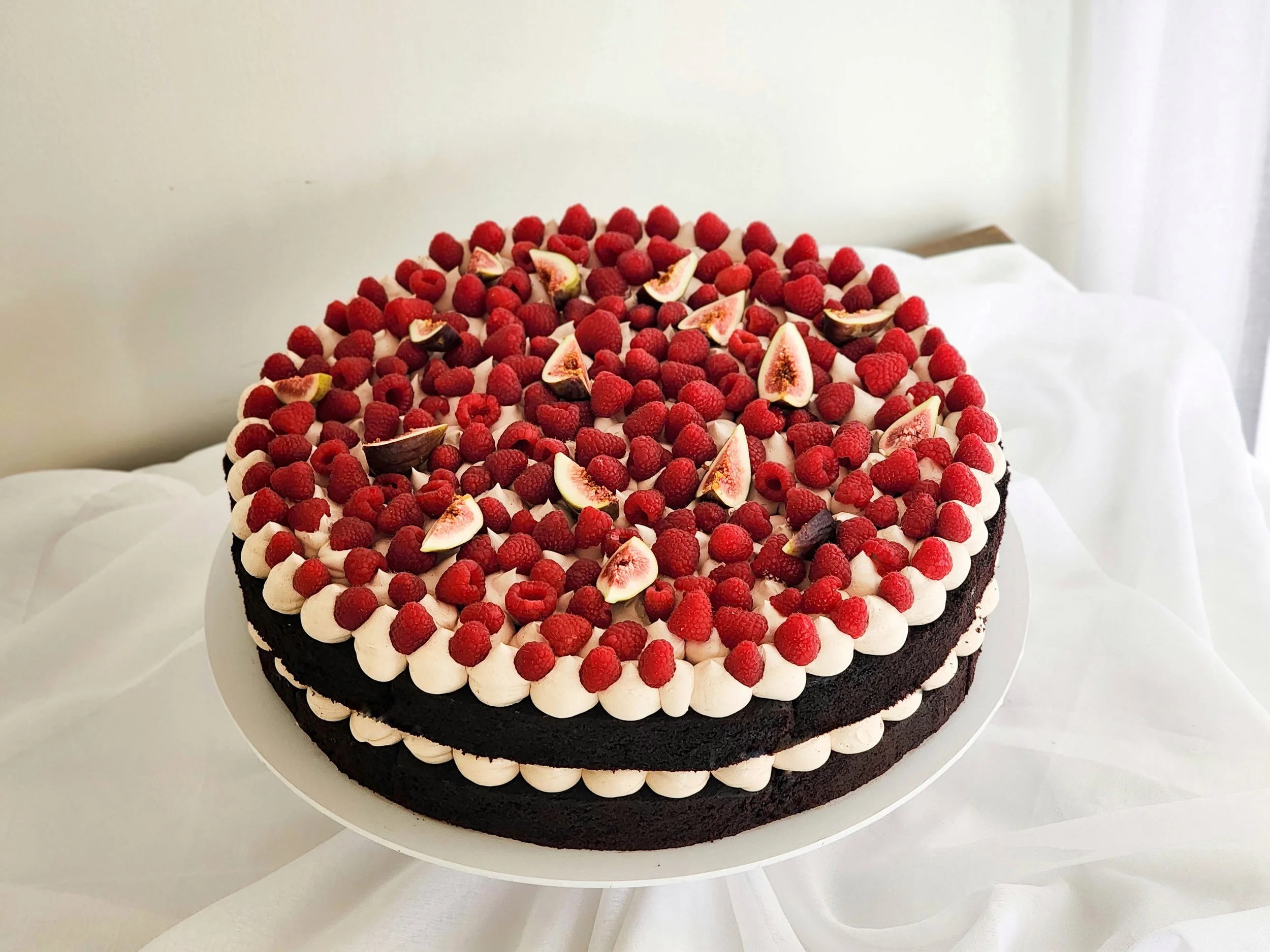 Chocolate layer cake with white frosting, topped with raspberries and fig slices on a white plate.