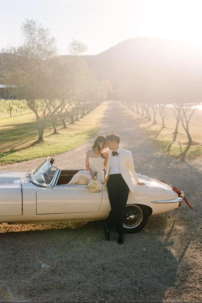 A bride and groom in a vintage car with vineyard backdrop