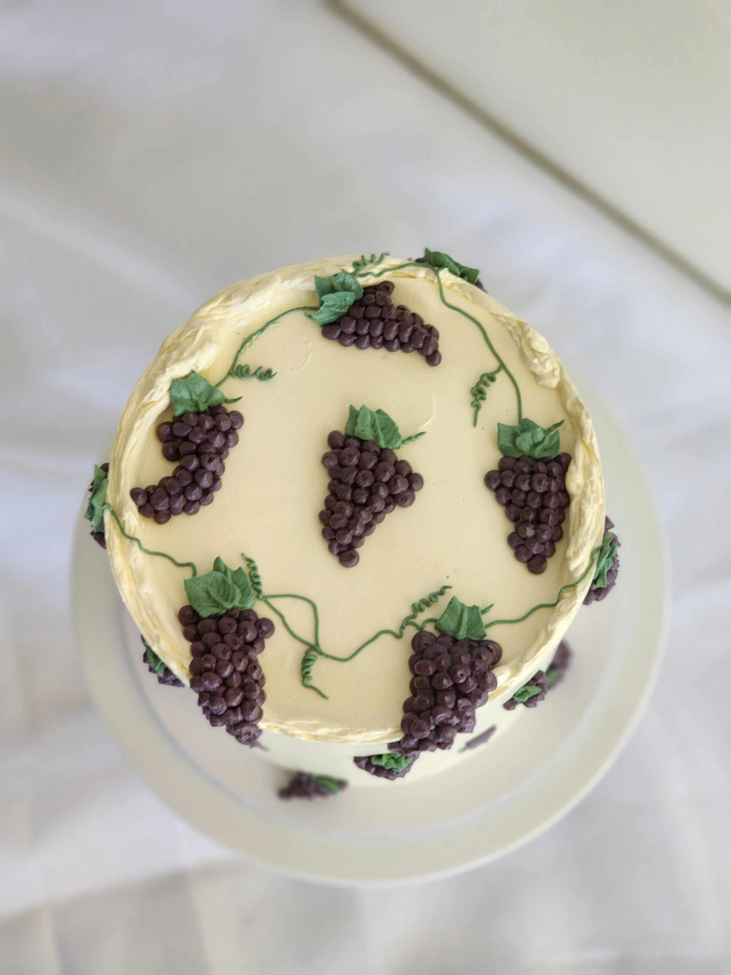 A white cake decorated with purple grape designs and green leaves.
