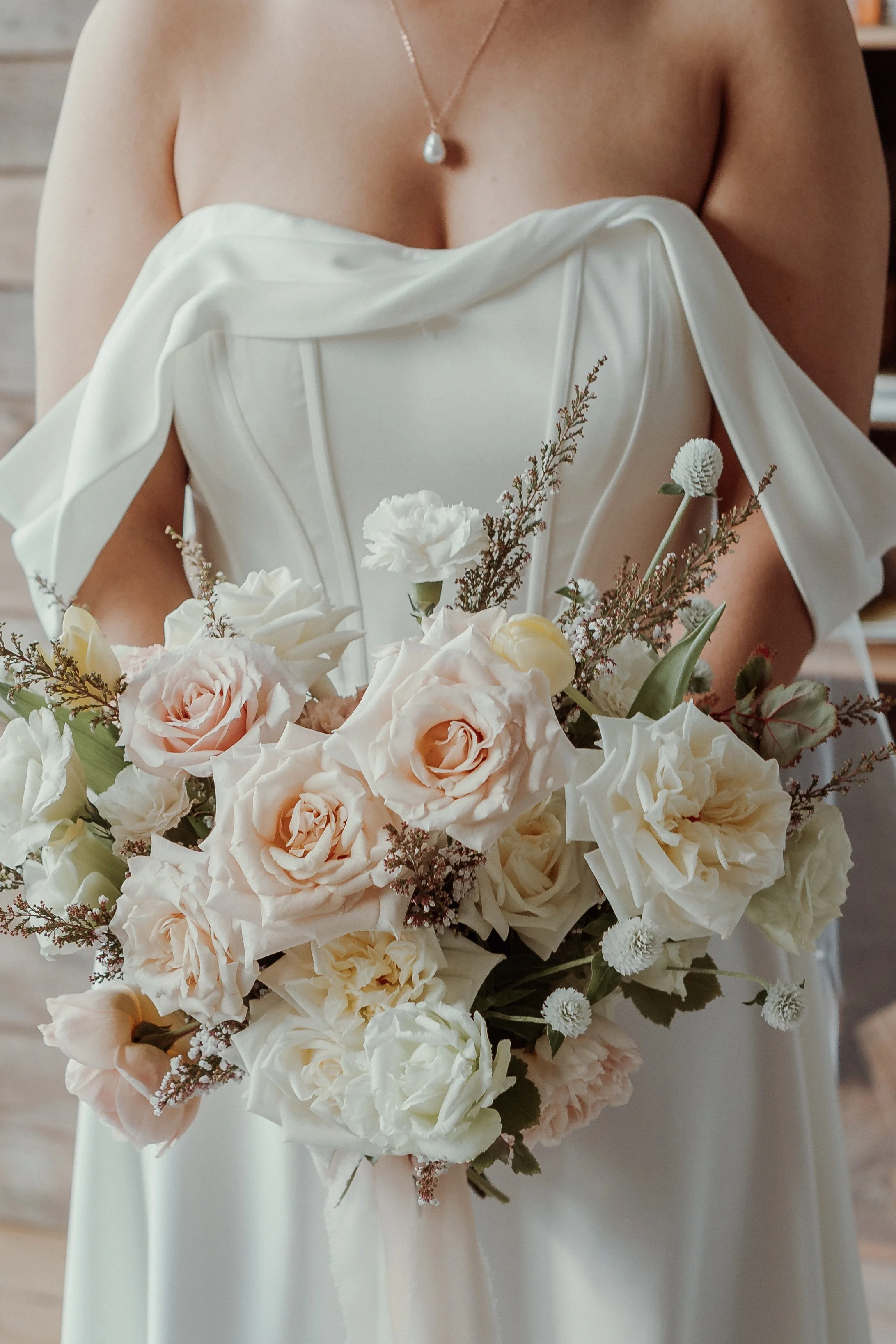 Bride in a white dress holding a bouquet of white and pale pink roses.