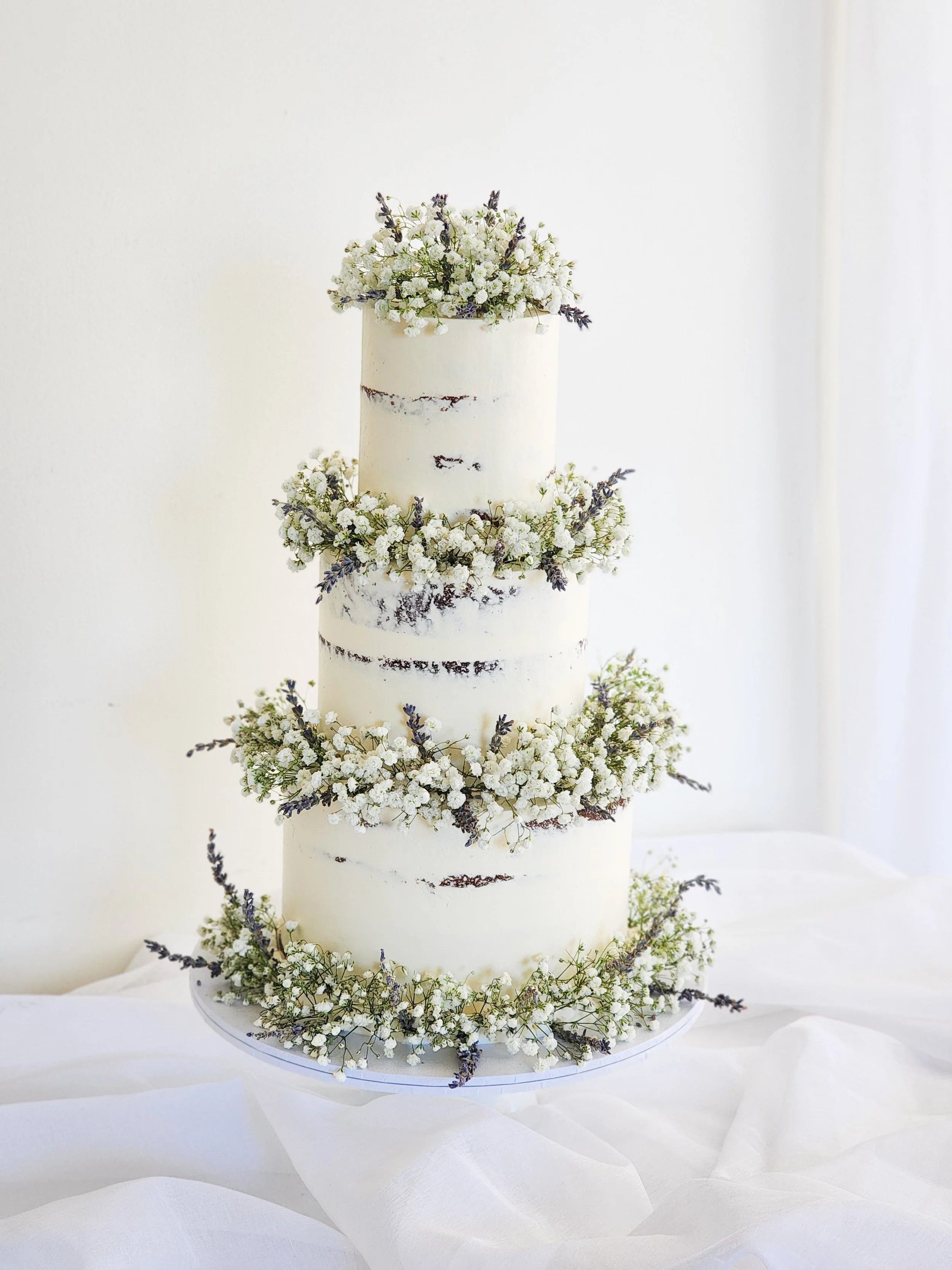 Three-tier white wedding cake decorated with baby's breath and lavender flowers.