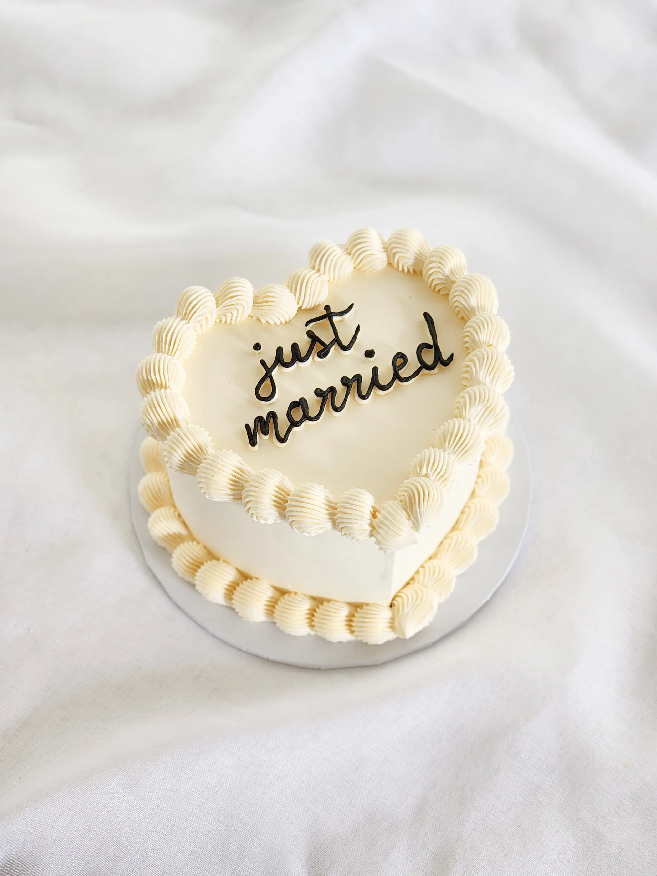 Heart-shaped wedding cake with white icing and piped cream border, decorated with the words "just married" in black icing.