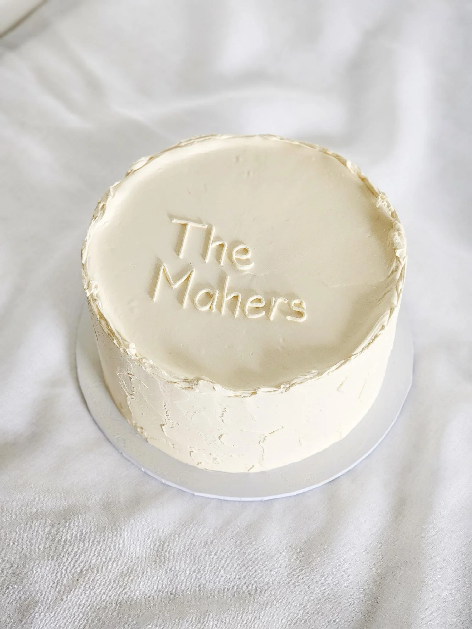A white frosted cake with the words "The Mahers" inscribed on the top.
