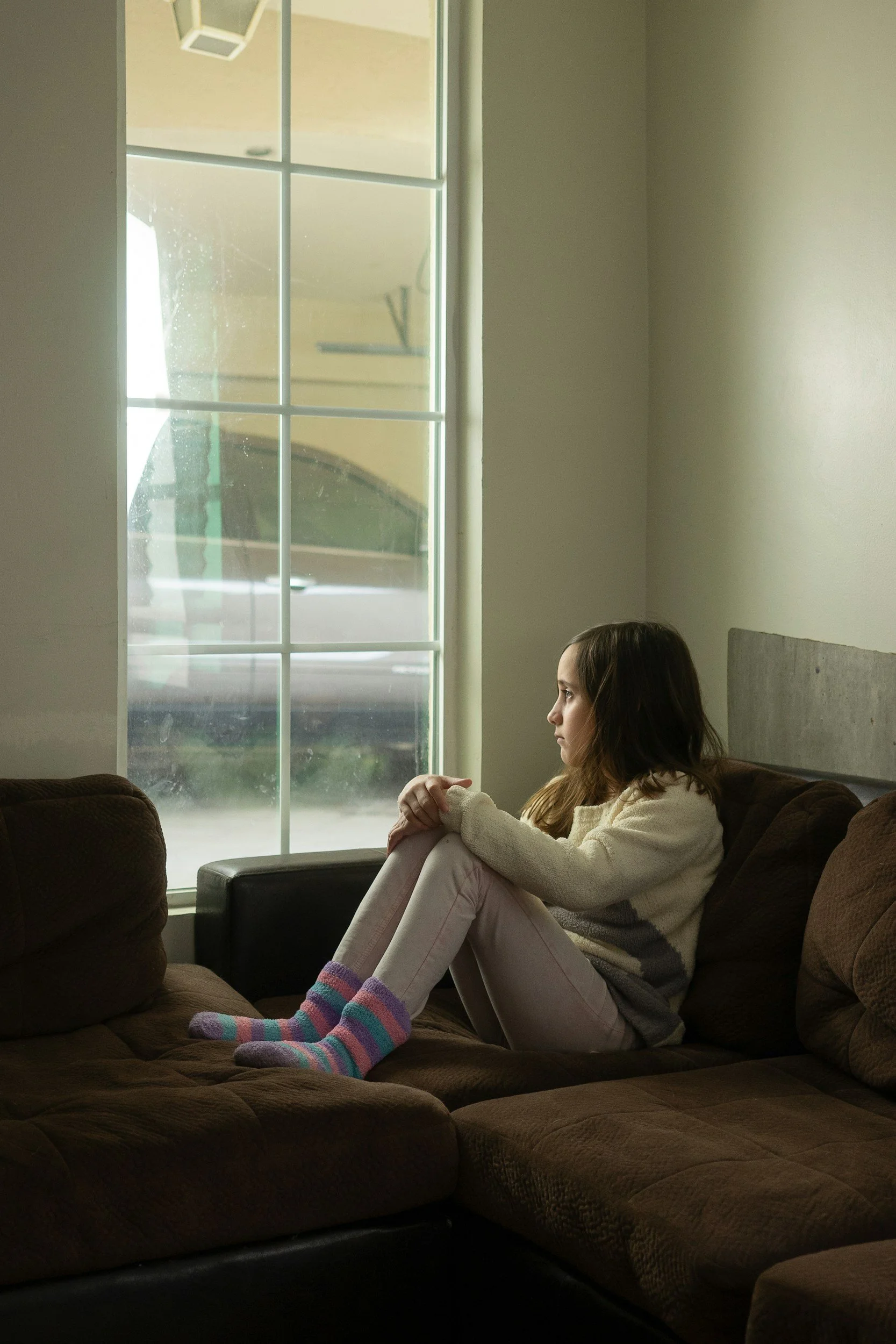 Young girl standing alone at a window, representing how childhood experiences can affect adult relationships and marriage.