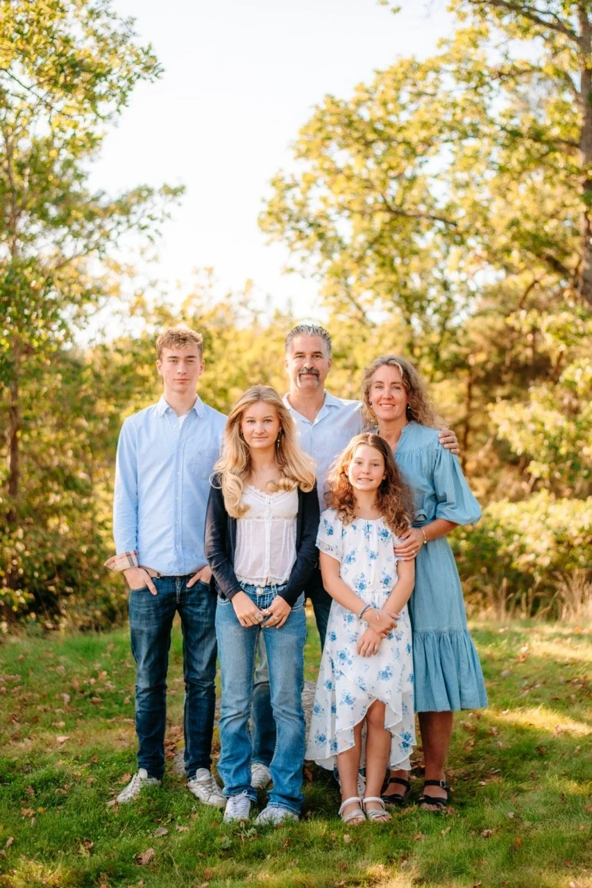 En familj på fem står tillsammans på en gräsmatta i en park med höstfärger.