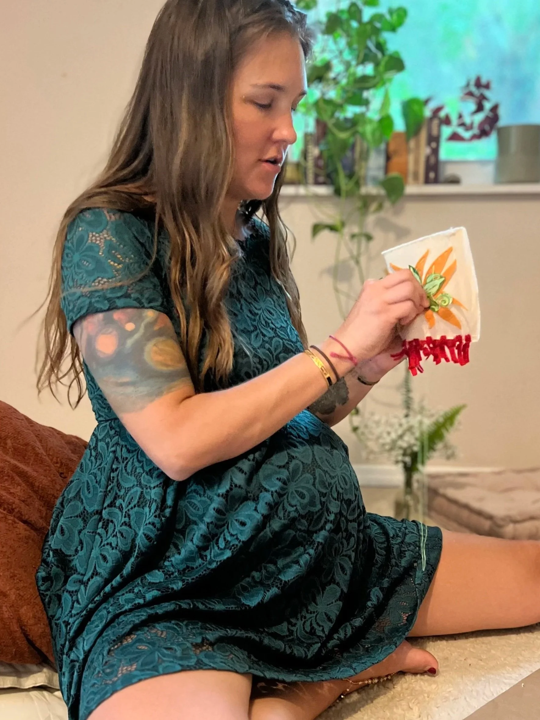 Pregnant birth doula stitching a handmade prayer flag during a mother blessing gathering.