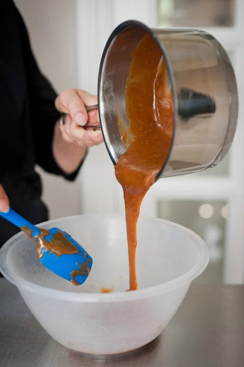 Hot caramel sauce being poured from a saucepan into a mixing bowl.