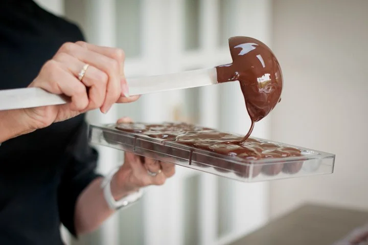Person pouring melted chocolate into a mold for making chocolates.