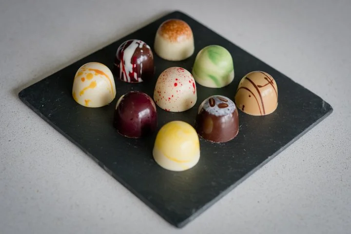 A black slate platter with ten assorted colorful chocolates arranged in two rows on a light gray surface.