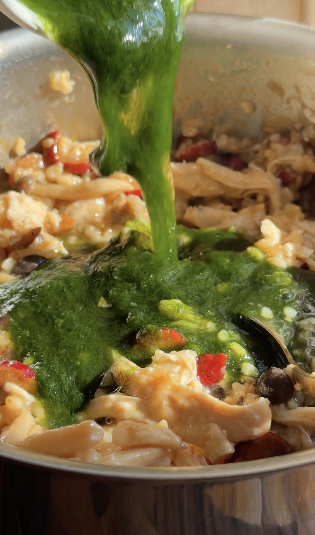 Vibrant green Maesaengi (Seaweed Fulvescens) being poured into a pot of Jook (Korean porridge) with shredded chicken and mushrooms.