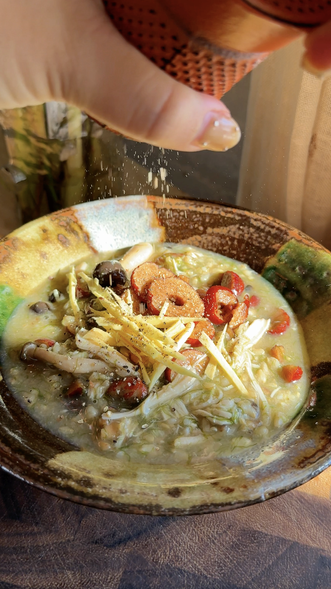 Fresh black pepper being ground over a bowl of Maesaengi-jook (Korean seaweed porridge) topped with ginger, jujubes, and mushrooms.