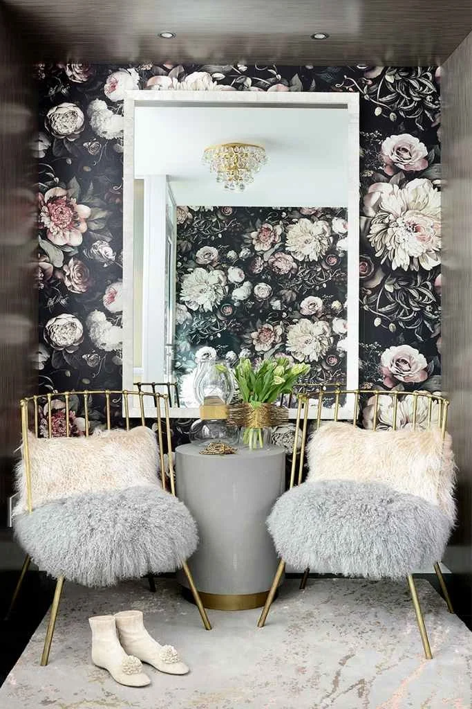 Chic entryway with a bespoke rug featuring delicate floral patterns, set beneath a glamorous mirror and flanked by plush chairs.
