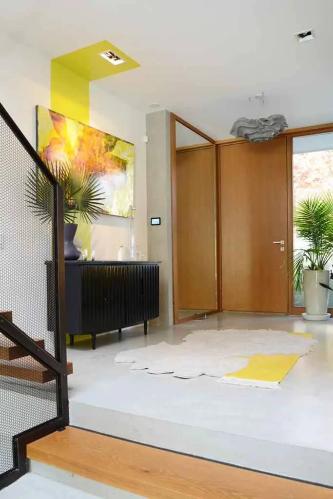 Bright entryway with a unique white and yellow bespoke rug, modern art, and vibrant plant decor.